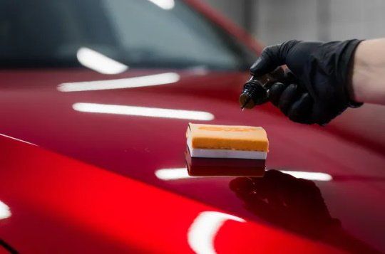 A person is polishing the hood of a red car with a sponge.