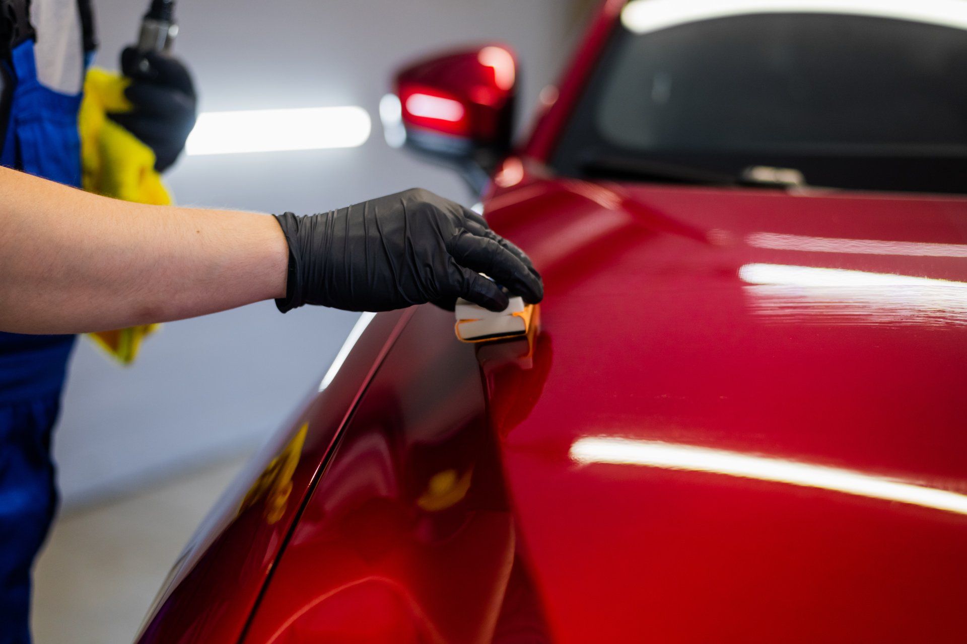 A person wearing black gloves is polishing a red car.
