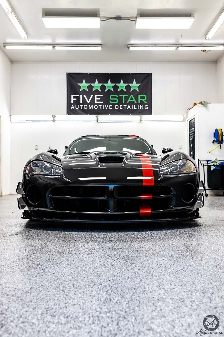 A black sports car is parked in a garage under a five star banner.