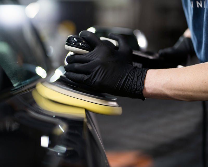 A person wearing black gloves is polishing a car with a machine.