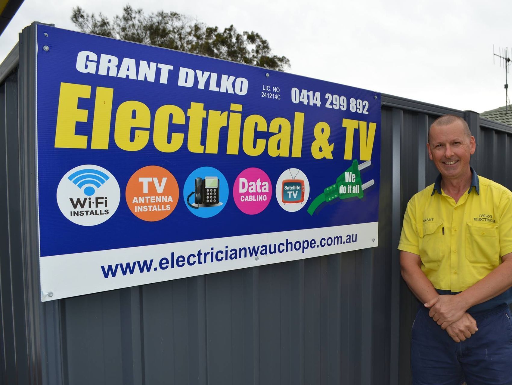 A man is standing in front of a sign for grant dylko electrical & tv — Dylko Electrical in Wauchope, NSW