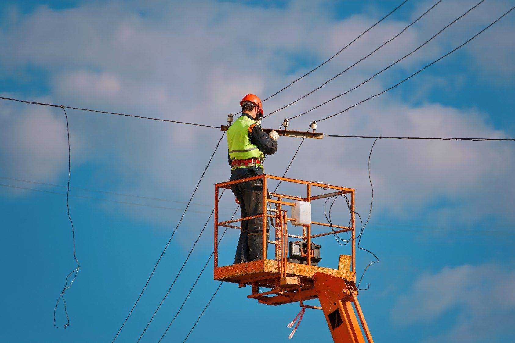 A Man is Standing in a Bucket on Top of a Crane Working on Power Lines — Dylko Electrical in Wauchope, NSW