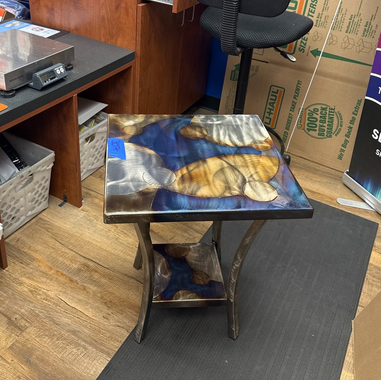 A square accent table with a live-edge wood top and shelf embedded in blue-swirled resin, set on dark metal legs.