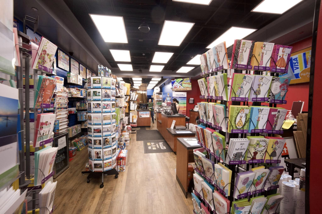 A retail store aisle featuring rows of greeting card racks and a checkout counter in the back.