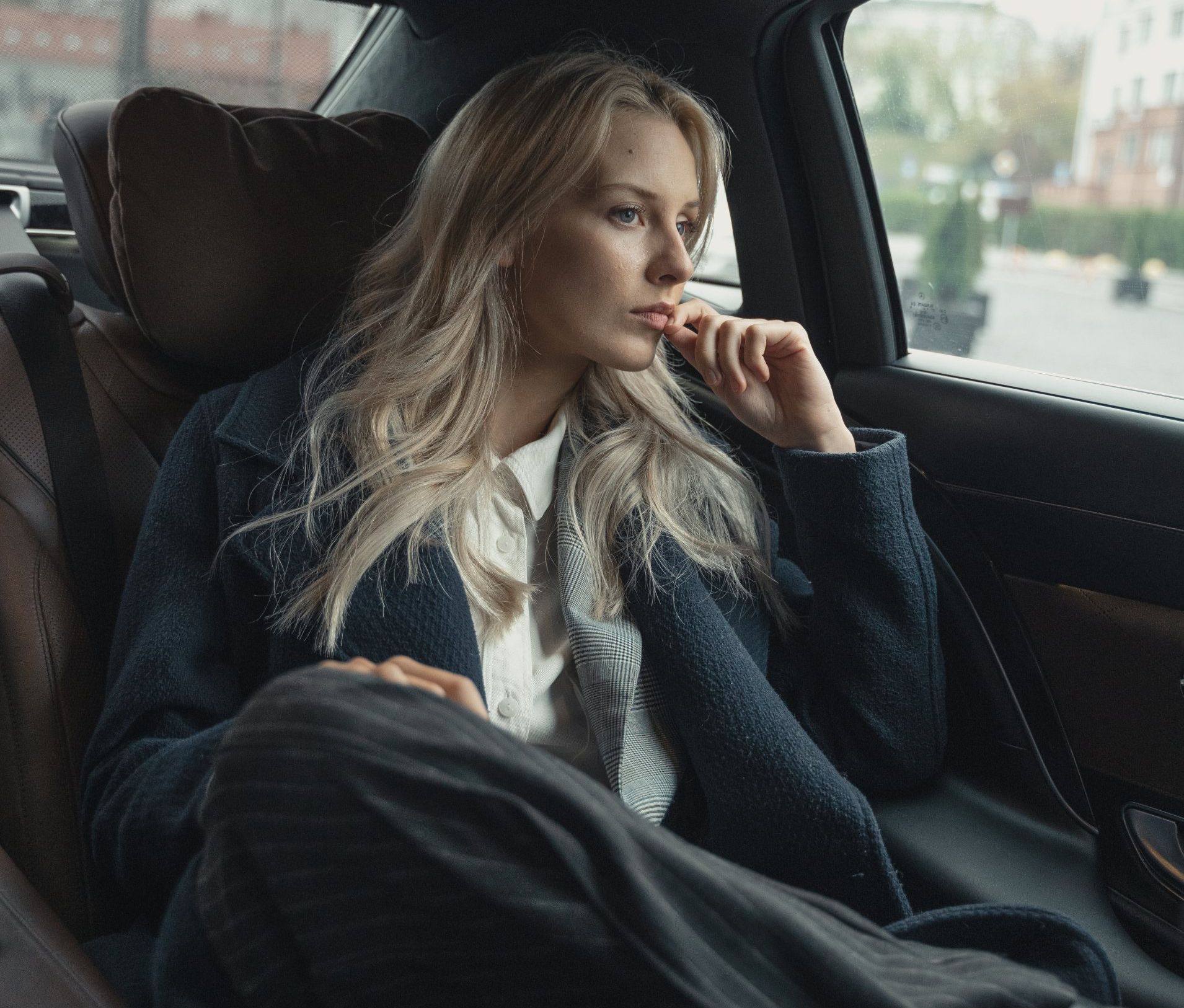 Female, blond, woman, CEO riding in the back of a car looking out the window with a pensive expression