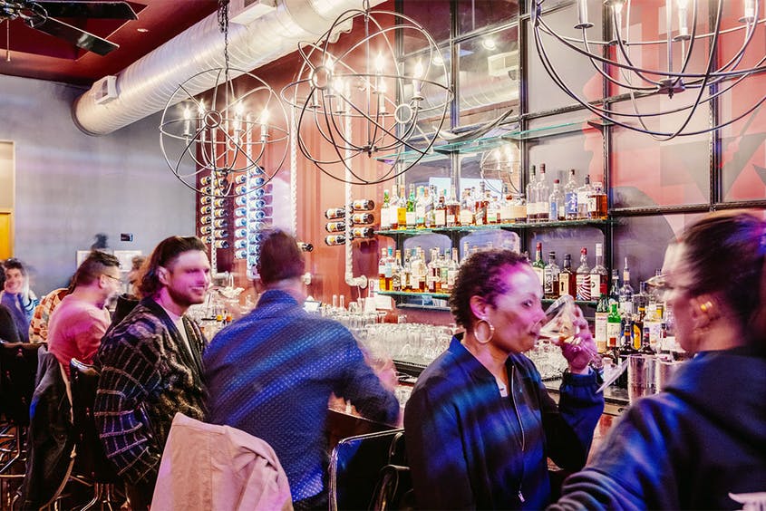 A group of people are sitting at a bar drinking wine.
