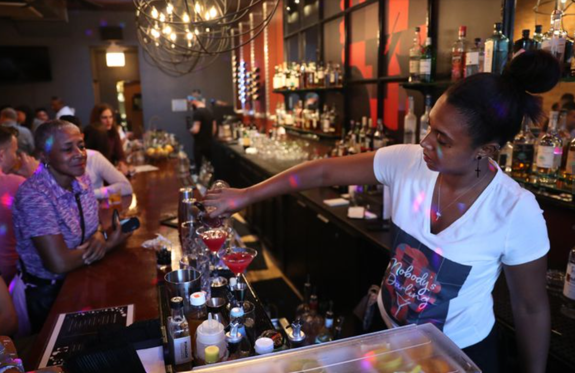 A woman is pouring a drink into a glass at a bar.