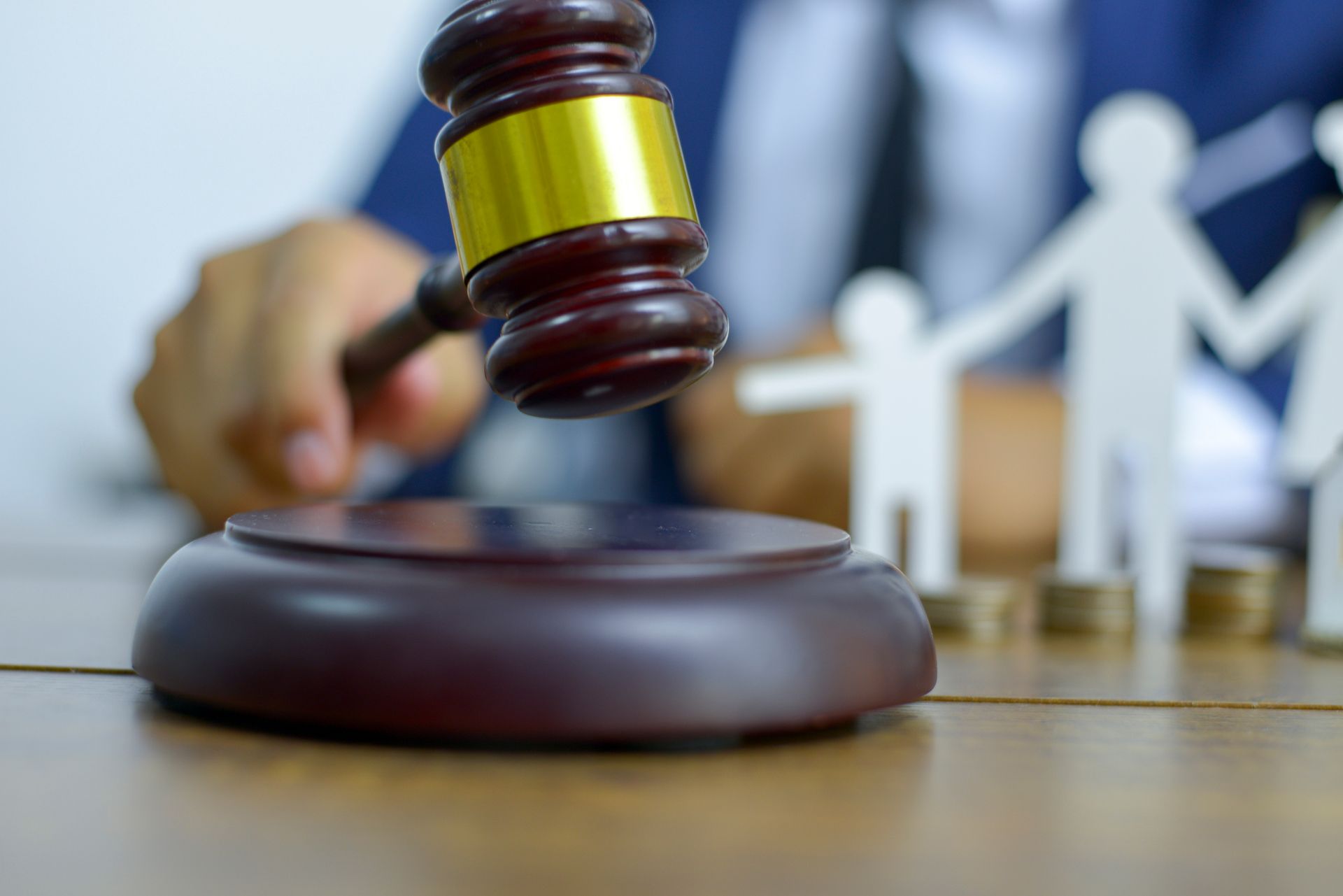 A family attorney in a blue suit holds a gavel on a table, with a family figure in the background. A family attorney in a blue suit holds a gavel on a table, with a family figure in the background.