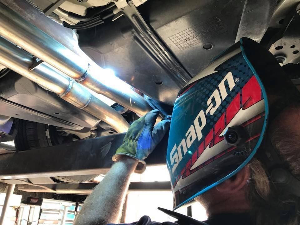 Mechanic in blue gloves working under a vehicle with a Snap-on welding helmet