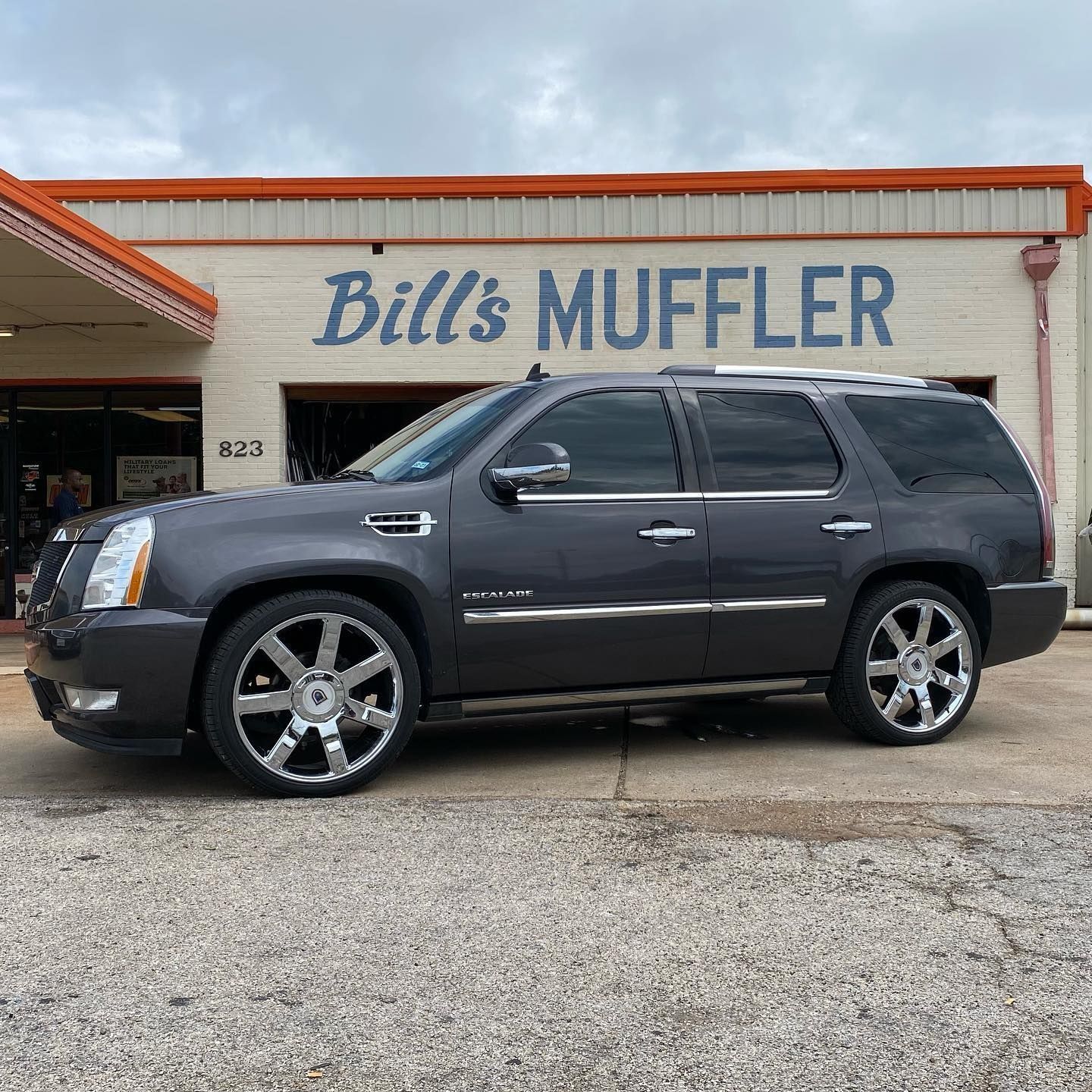 Gray SUV parked outside Bill’s Muffler shop with orange trim on the building