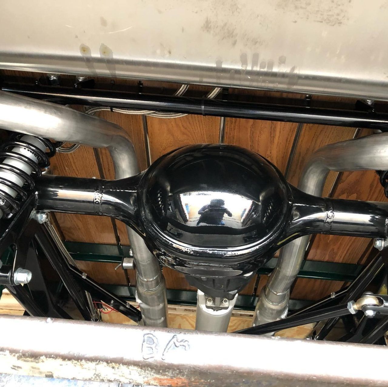 Black metal undercarriage assembly with coiled spring and chrome piping beneath a vehicle seat