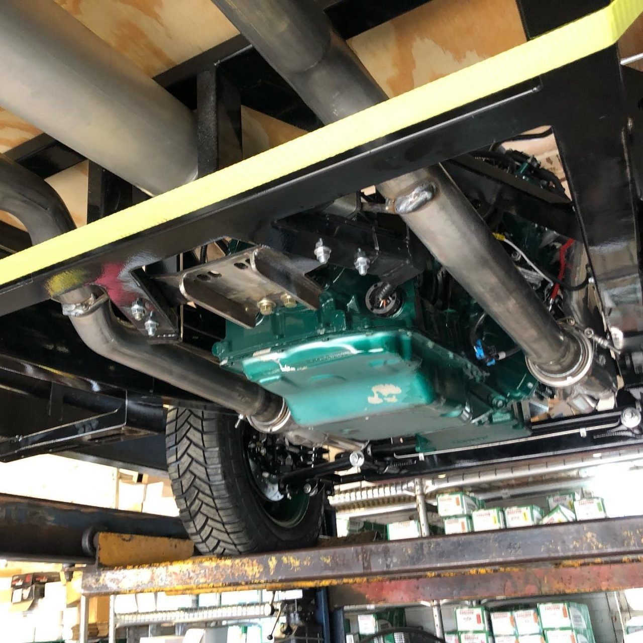 Underside of a green car on a lift, with exhaust pipes and frame visible in a garage or workshop.