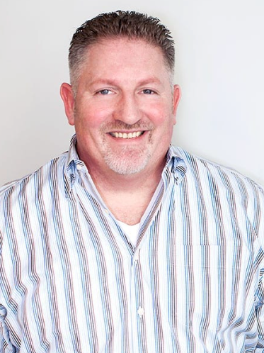 Man with short, styled hair, wearing a striped button-down shirt, smiling.