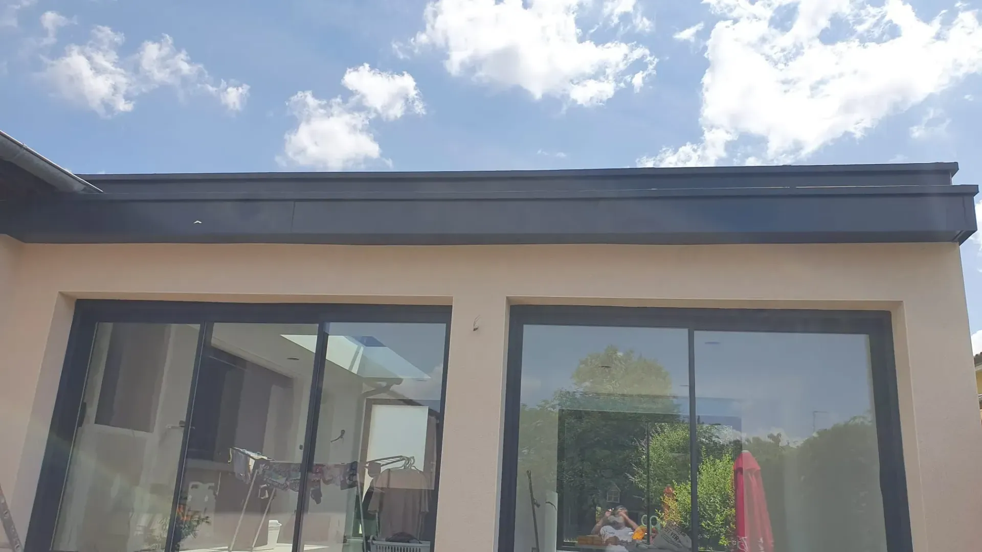 Vue en contre-plongée d'un bâtiment beige avec deux grandes portes coulissantes en verre à cadre sombre sous une toiture noire.