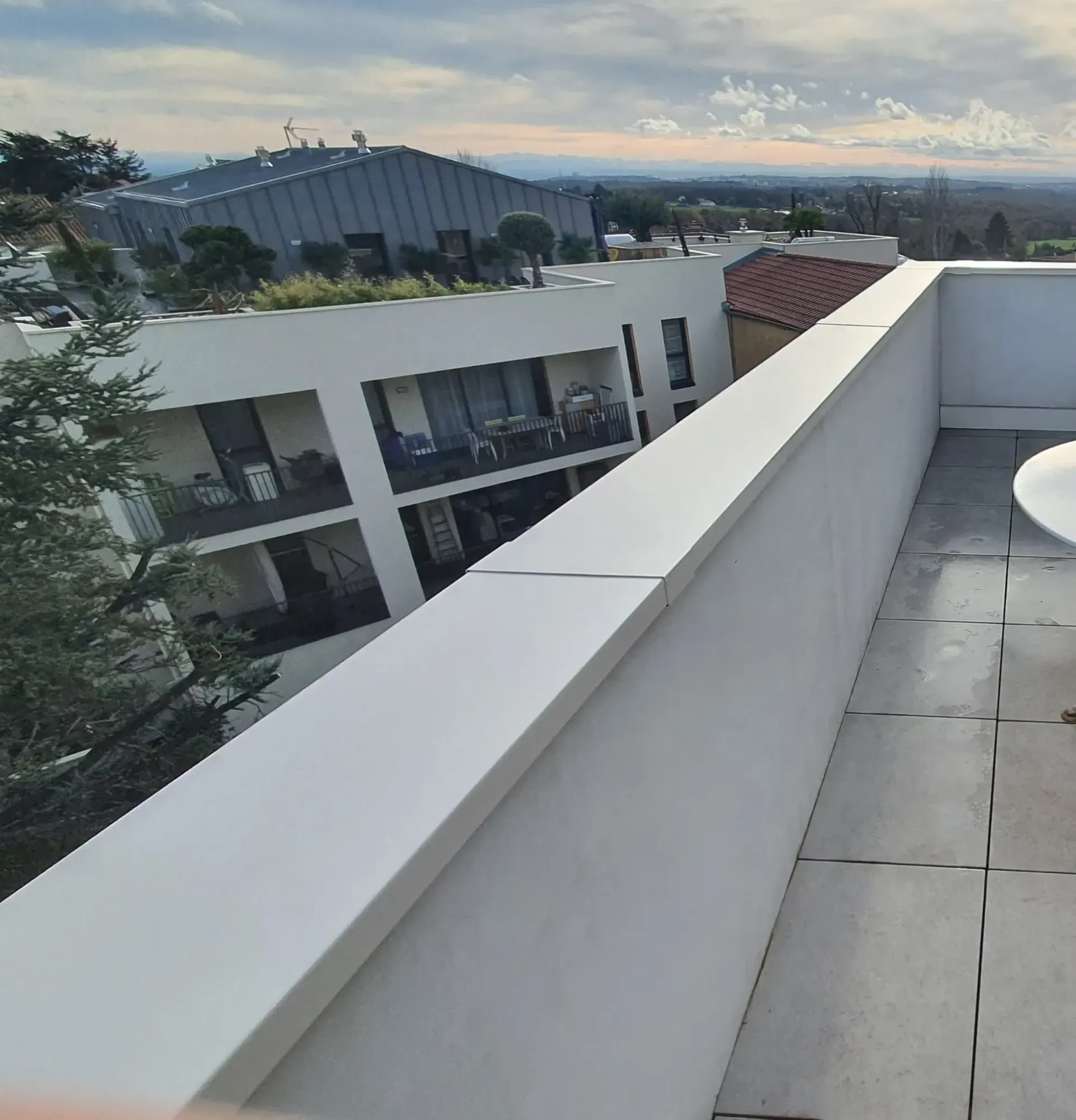 Vue en plongée d'une terrasse carrelée sur le toit d'un immeuble d'appartements blanc moderne et sur un horizon lointain.