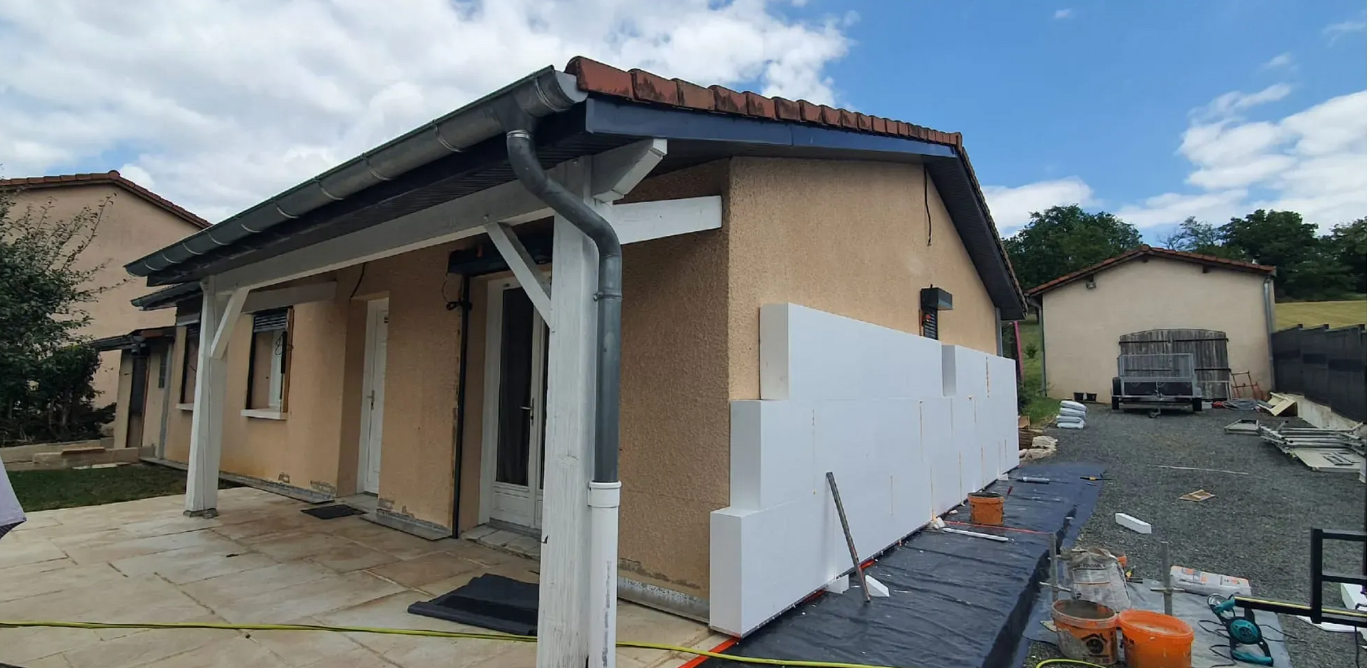 L'extérieur d'une maison en cours de rénovation, avec des panneaux d'isolation en mousse blanche partiellement installés sur le mur en stuc beige.