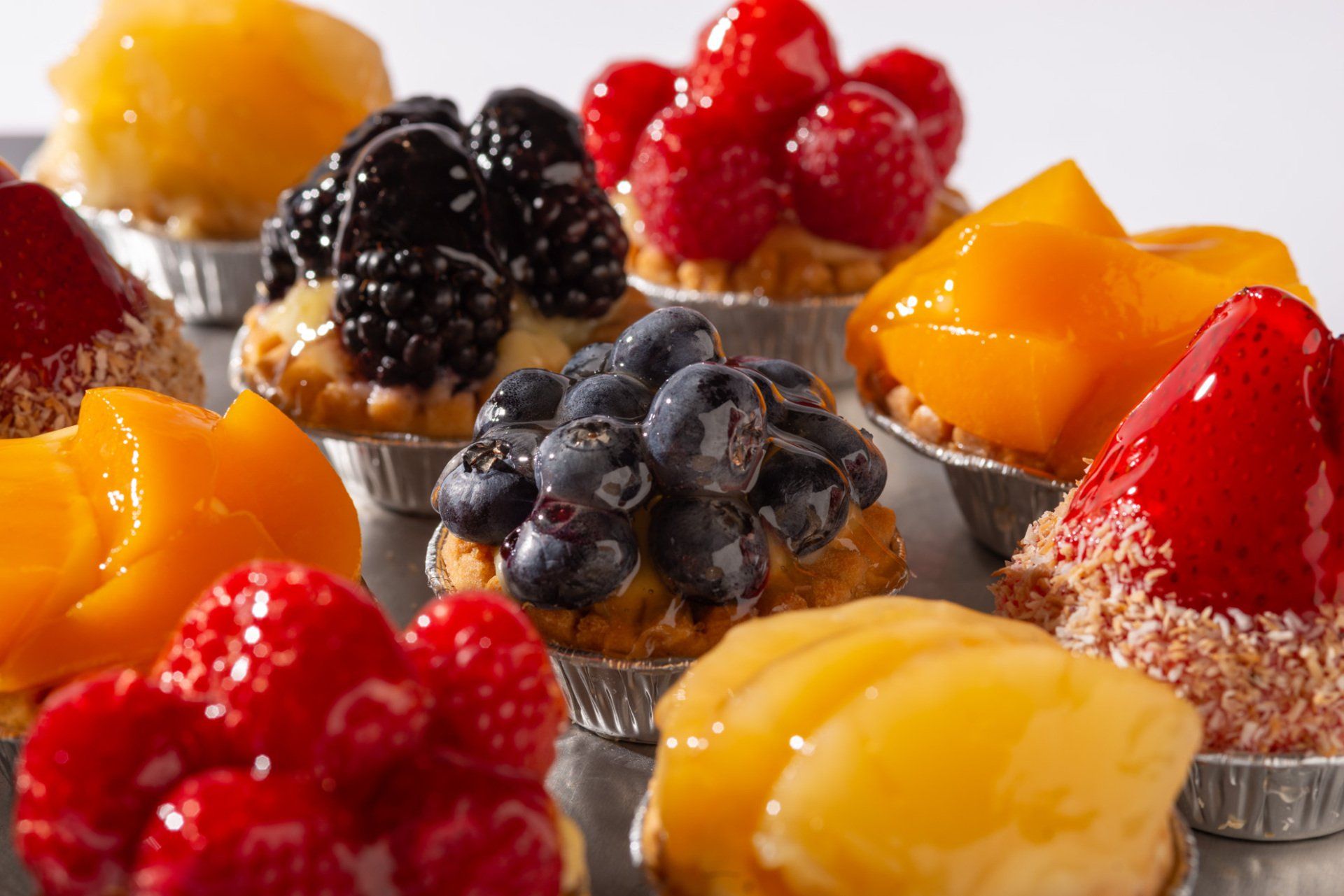 Assorted fruit tartlets with glossy berries and orange glaze on a white surface
