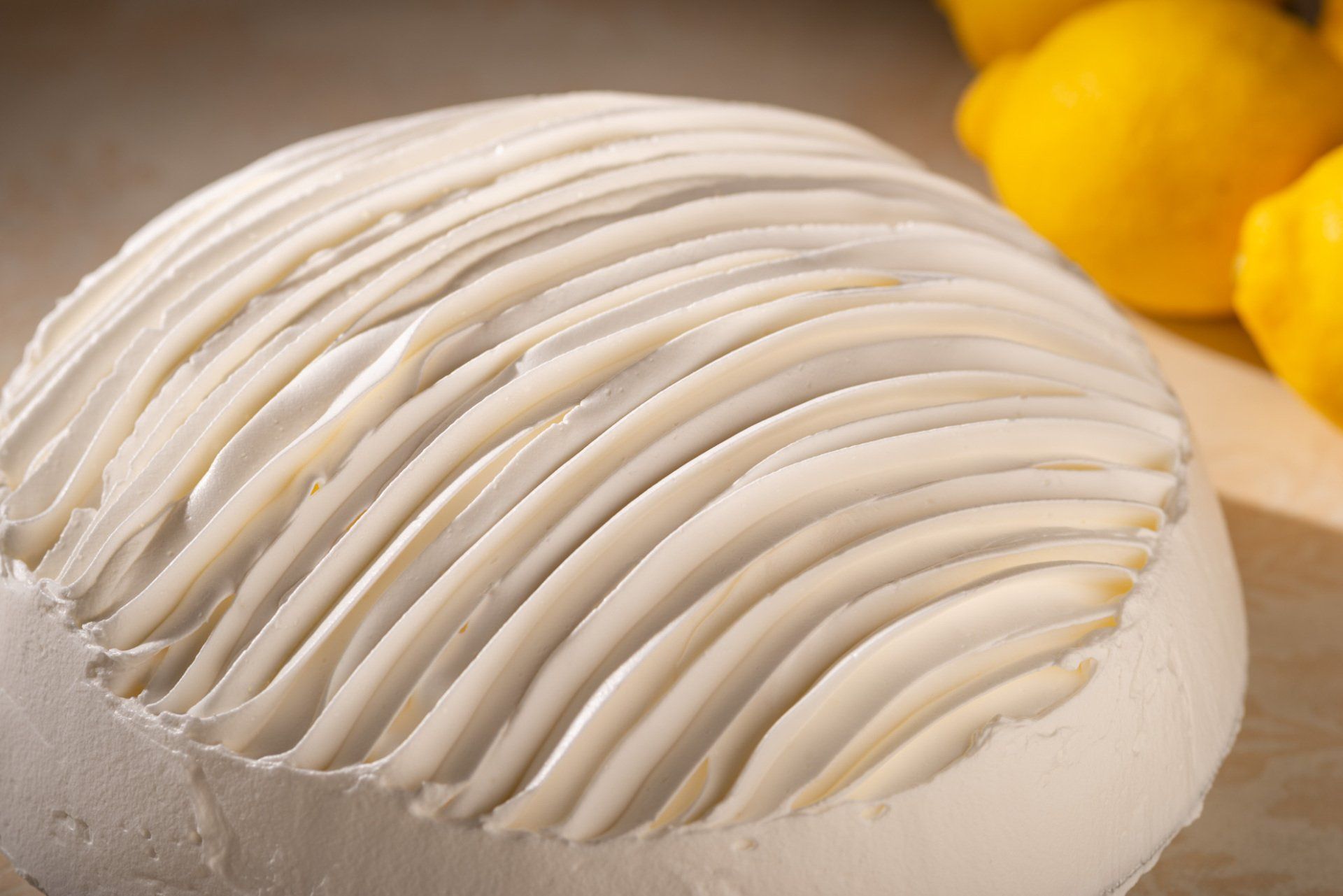 White meringue dessert with ridged top, garnished with lemon slices on a beige surface