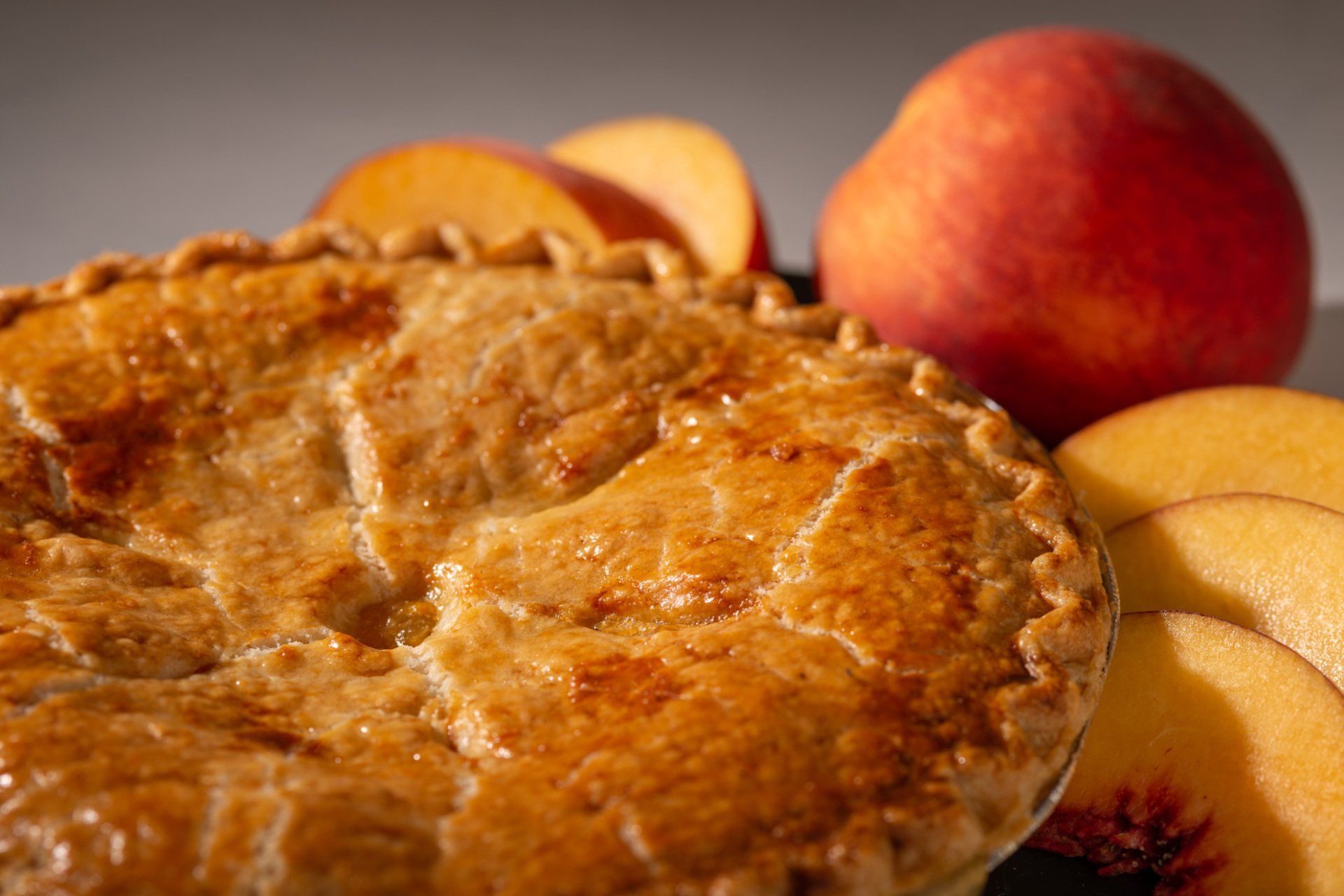 Golden-brown pie with peaches and a peach in the background