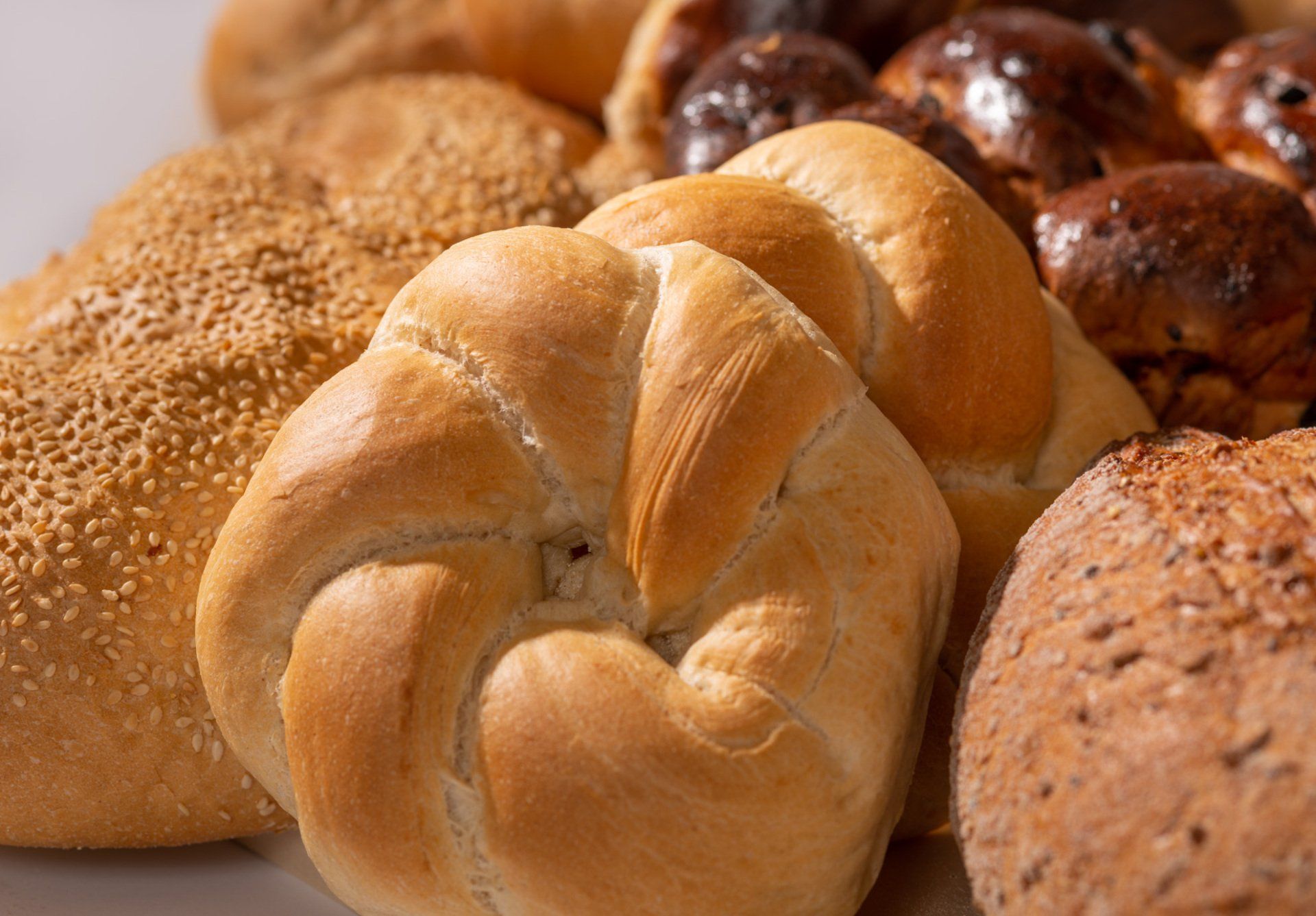 Assorted fresh bread rolls and loaves, including a twisted bun in the foreground, on a bakery display