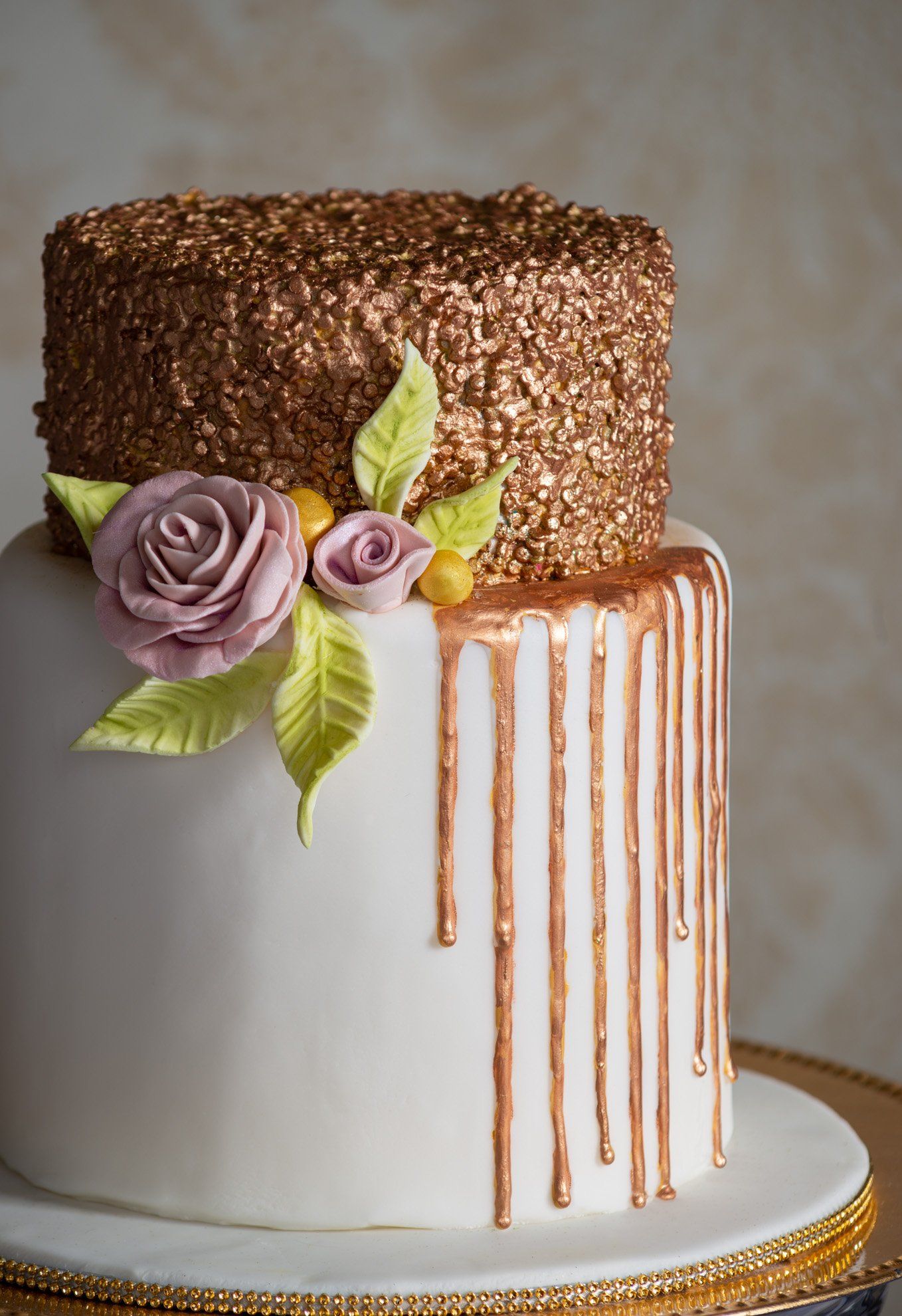 White cake with gold drip glaze, lavender roses, and a sparkling gold top on a cake stand