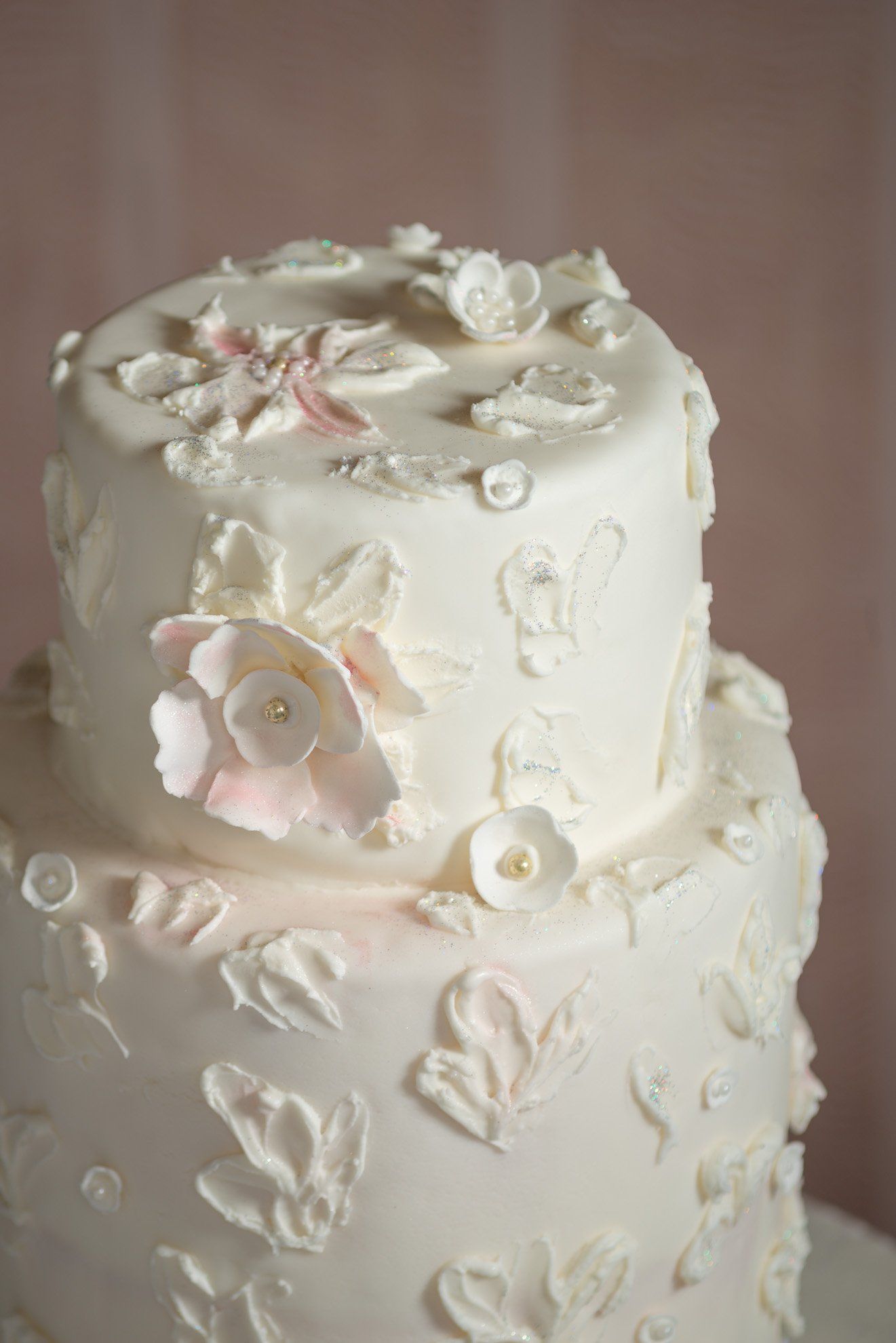 Two-tier white wedding cake with delicate floral decorations and a soft pink flower accent