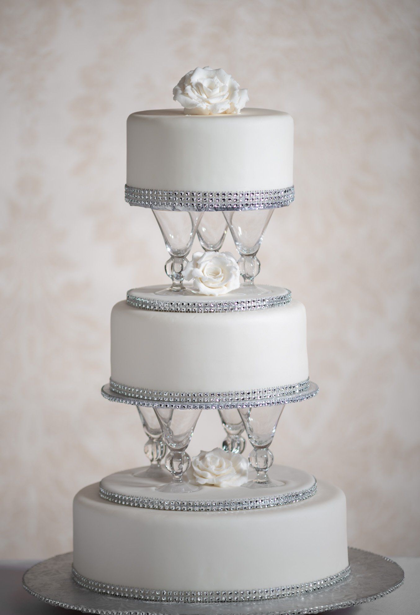 Three-tier white wedding cake with silver beading and clear crystal supports on a silver base.