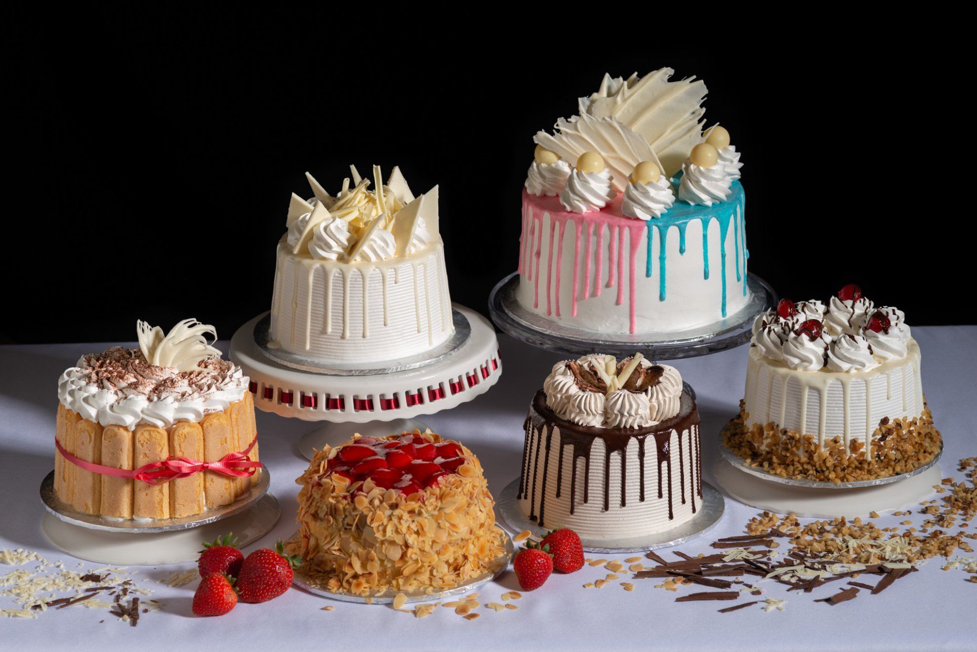 Six decorated layer cakes on a gray surface, with crumbs and berries scattered around.