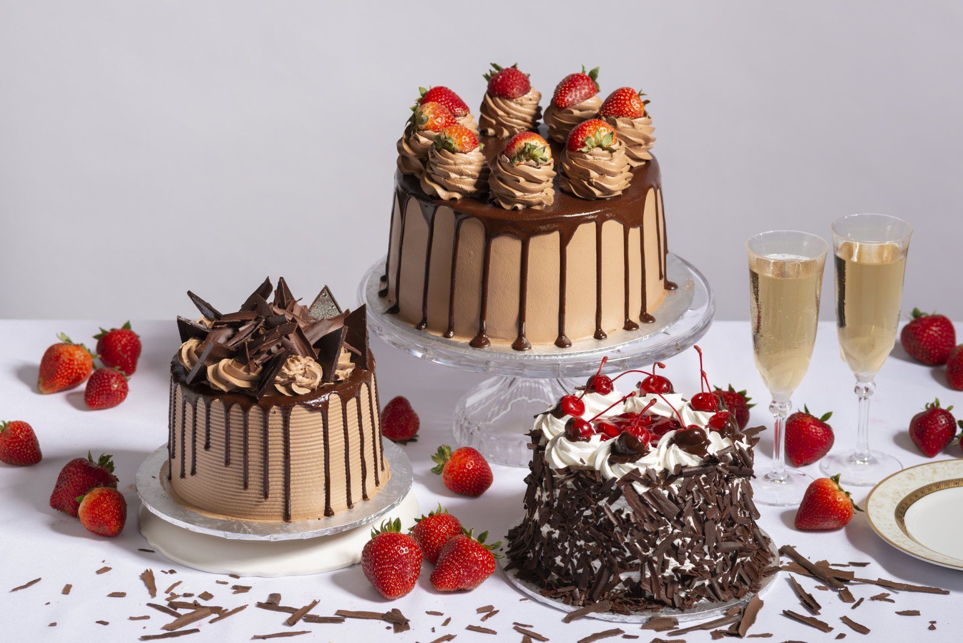 Chocolate cakes with strawberries and whipped cream on a white table, with two glasses of champagne