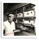Person in a bakery operating a large industrial oven with trays of bread or pastries