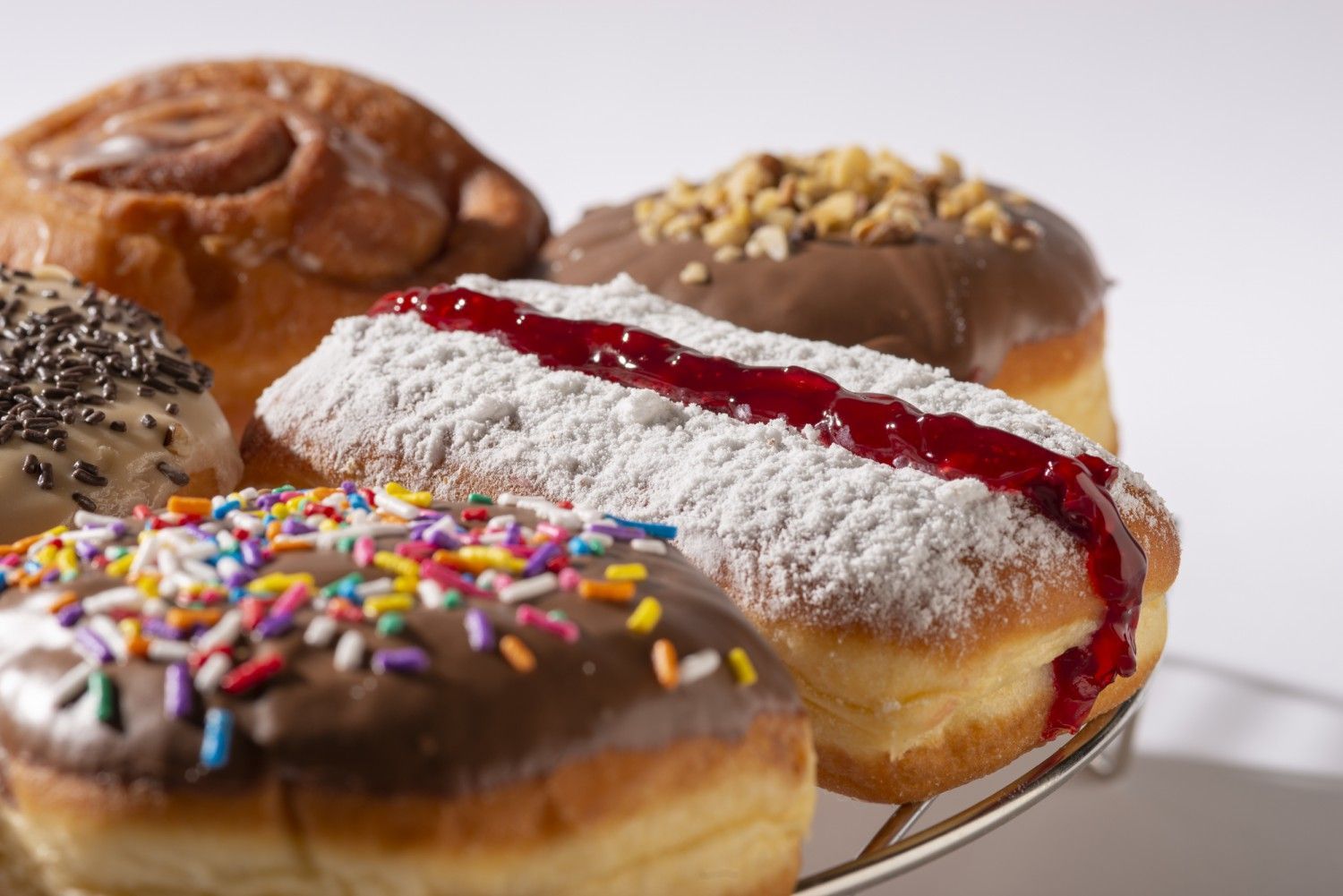 Assorted glazed donuts on a plate, including chocolate-frosted and jelly-filled varieties, with colorful sprinkles
