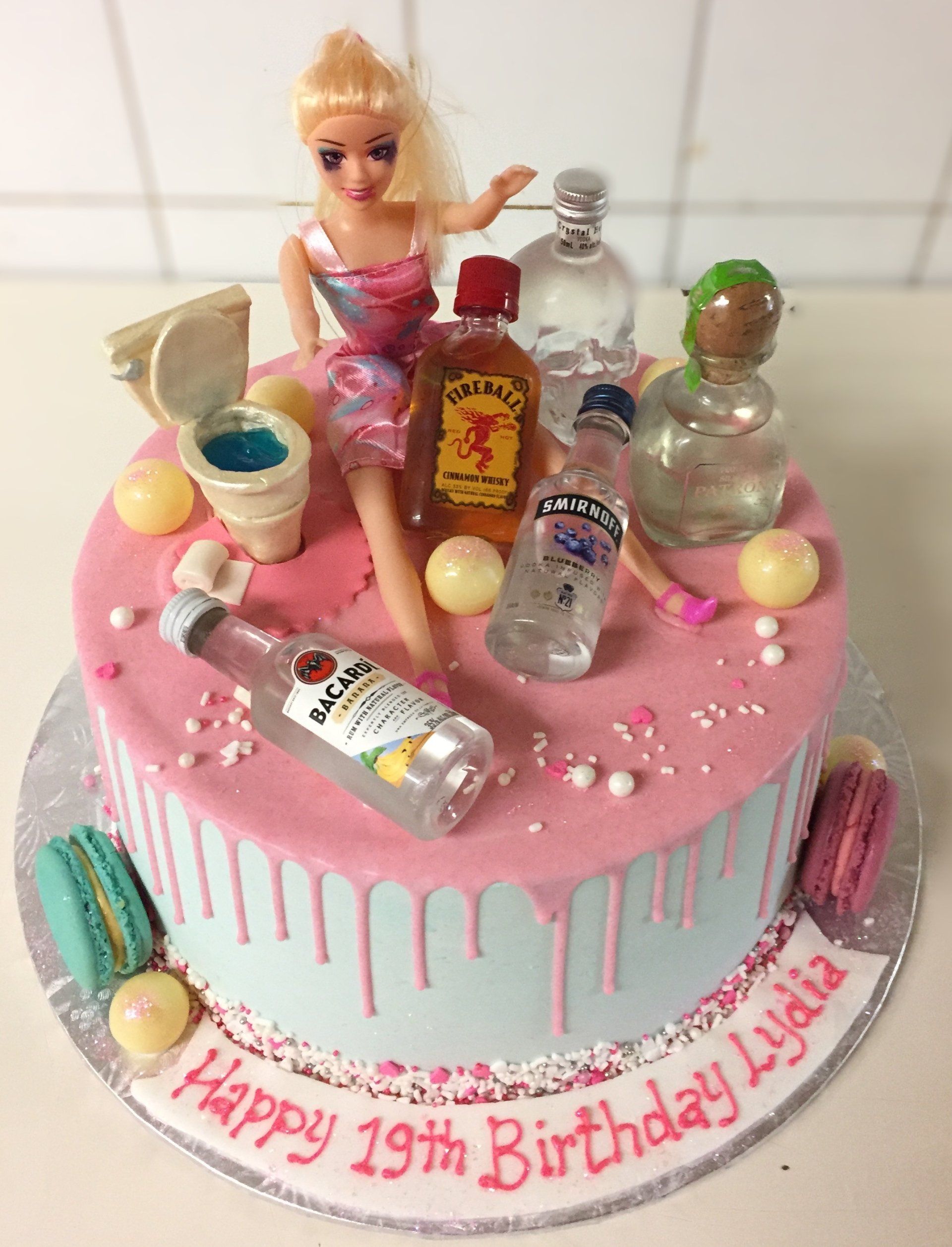 Pink birthday cake topped with doll and tiny bottles, decorated with “Happy 19th Birthday Kayla” icing.