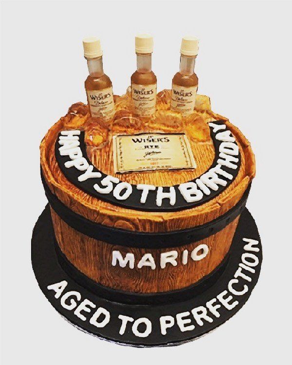 Round birthday cake with three bottles on top and “Happy 50th Birthday” and “Mario Aged to Perfection” written on it