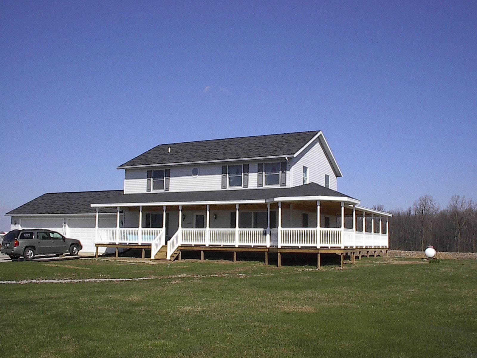 A white house with a large porch and a car parked in front of it