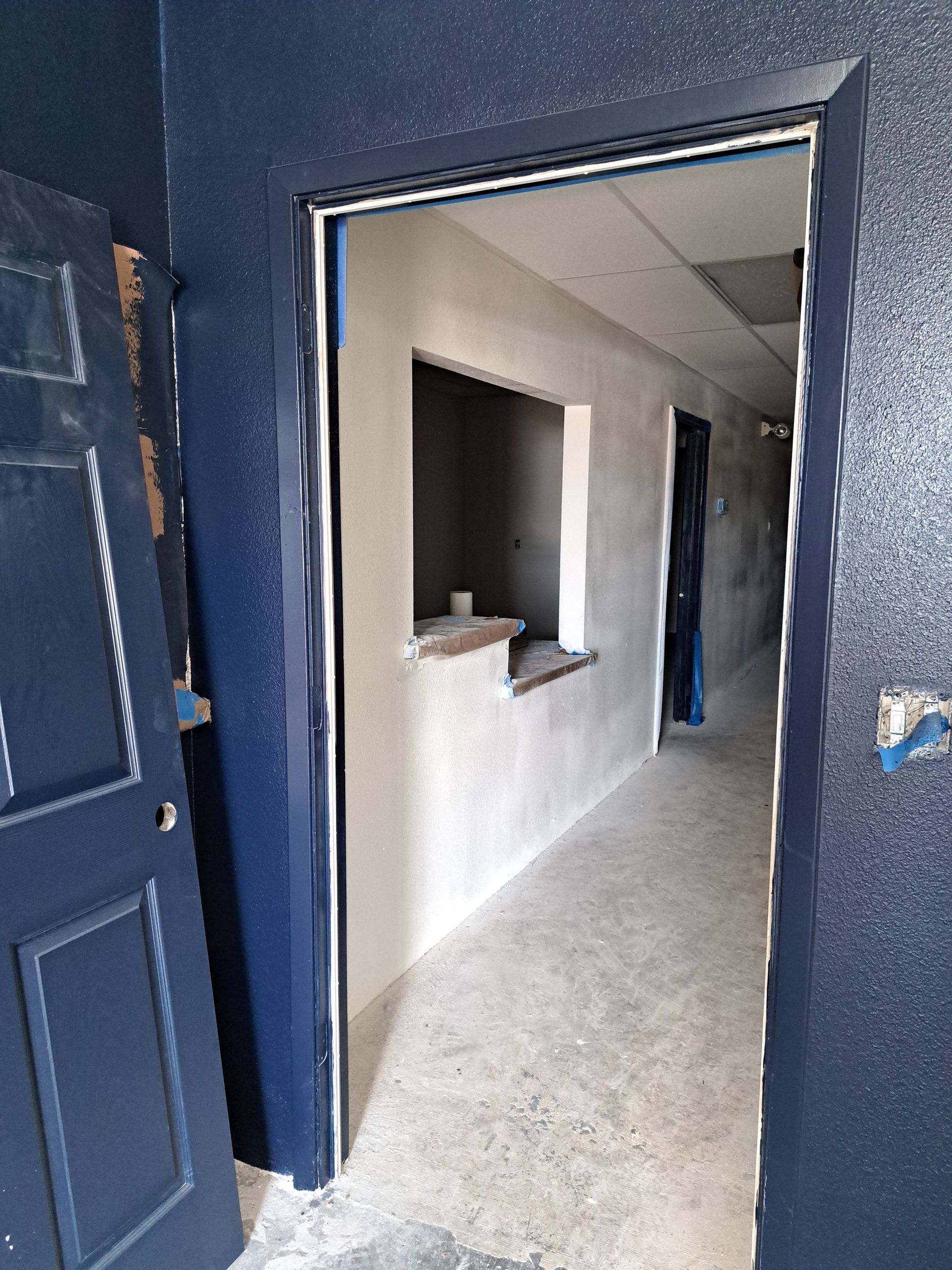 Interior hallway under construction, blue door frame, white walls, counter, and door.