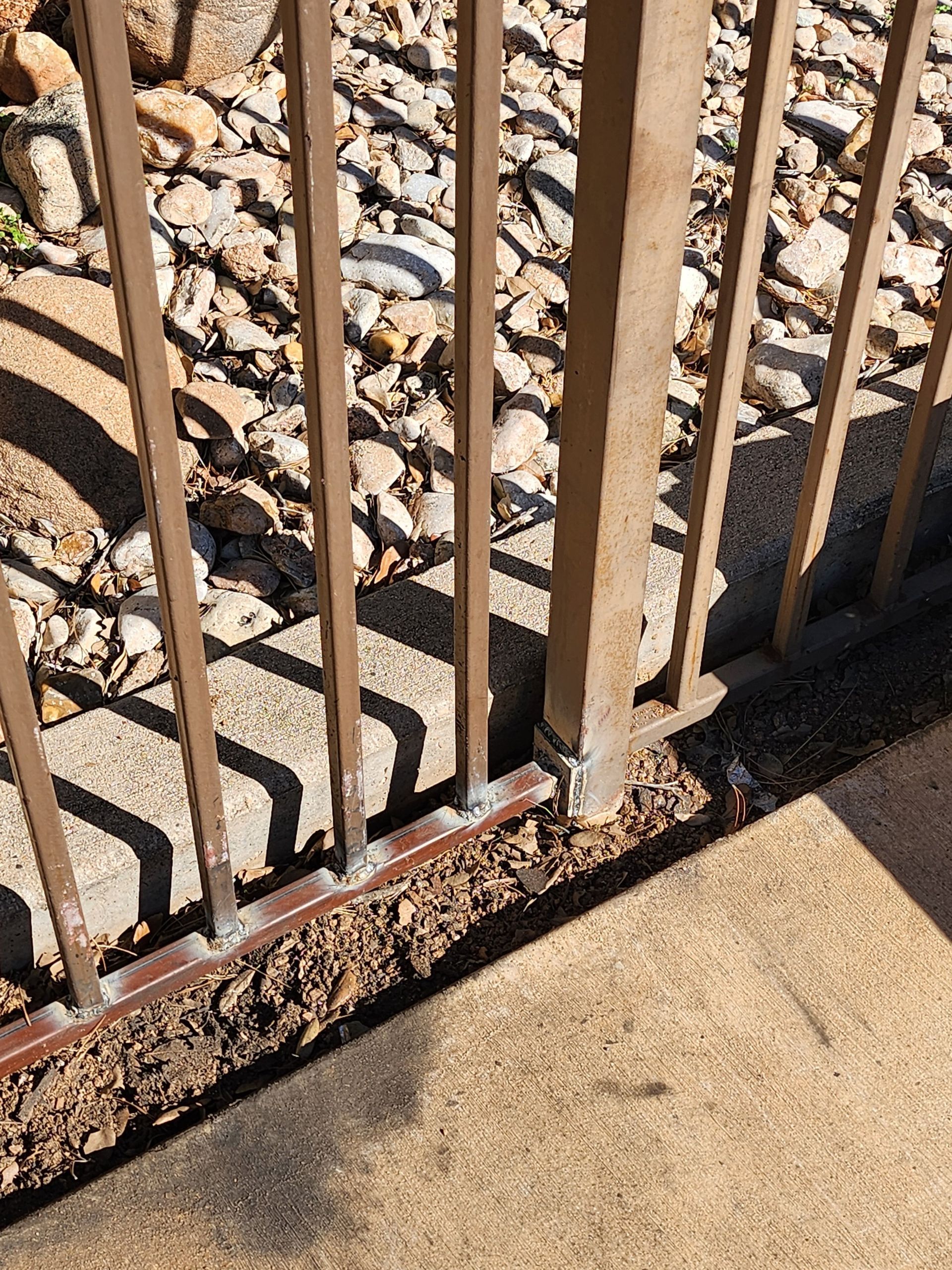 Brown metal fence on concrete surface with gravel background.