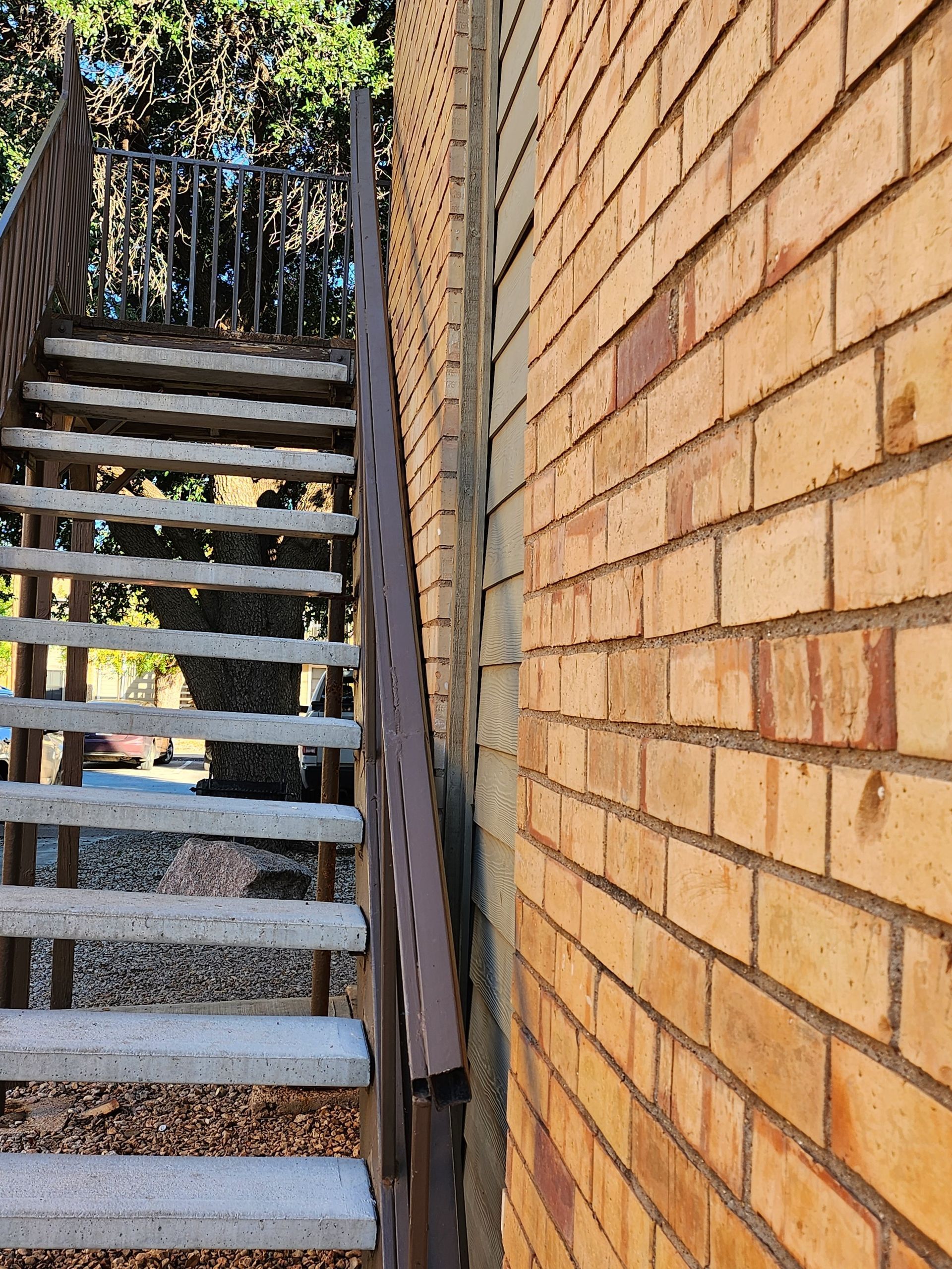 Exterior staircase next to brick wall, with a brown metal handrail.