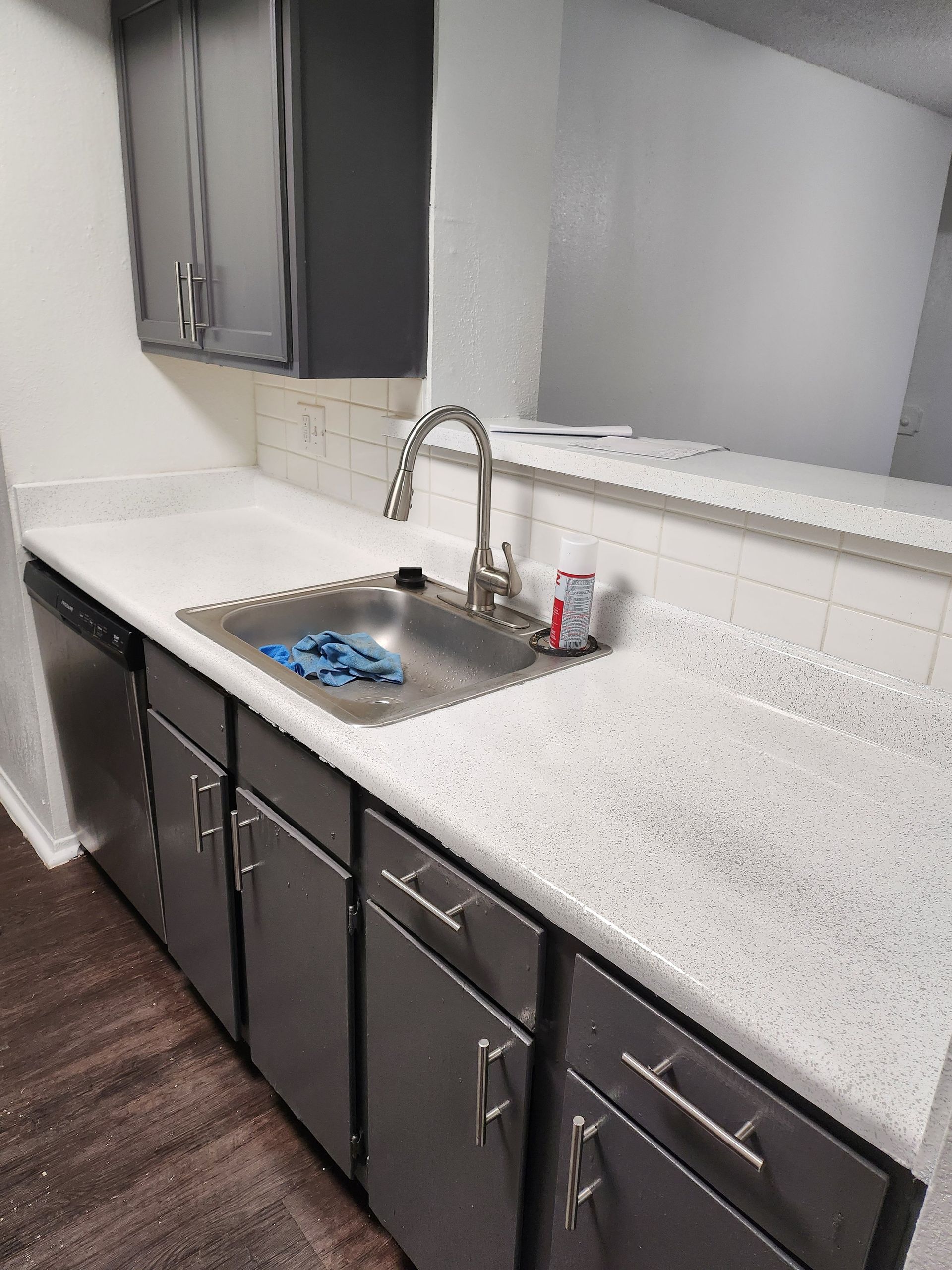 Kitchen with stainless steel sink, gray cabinets, white countertop, and silver faucet.