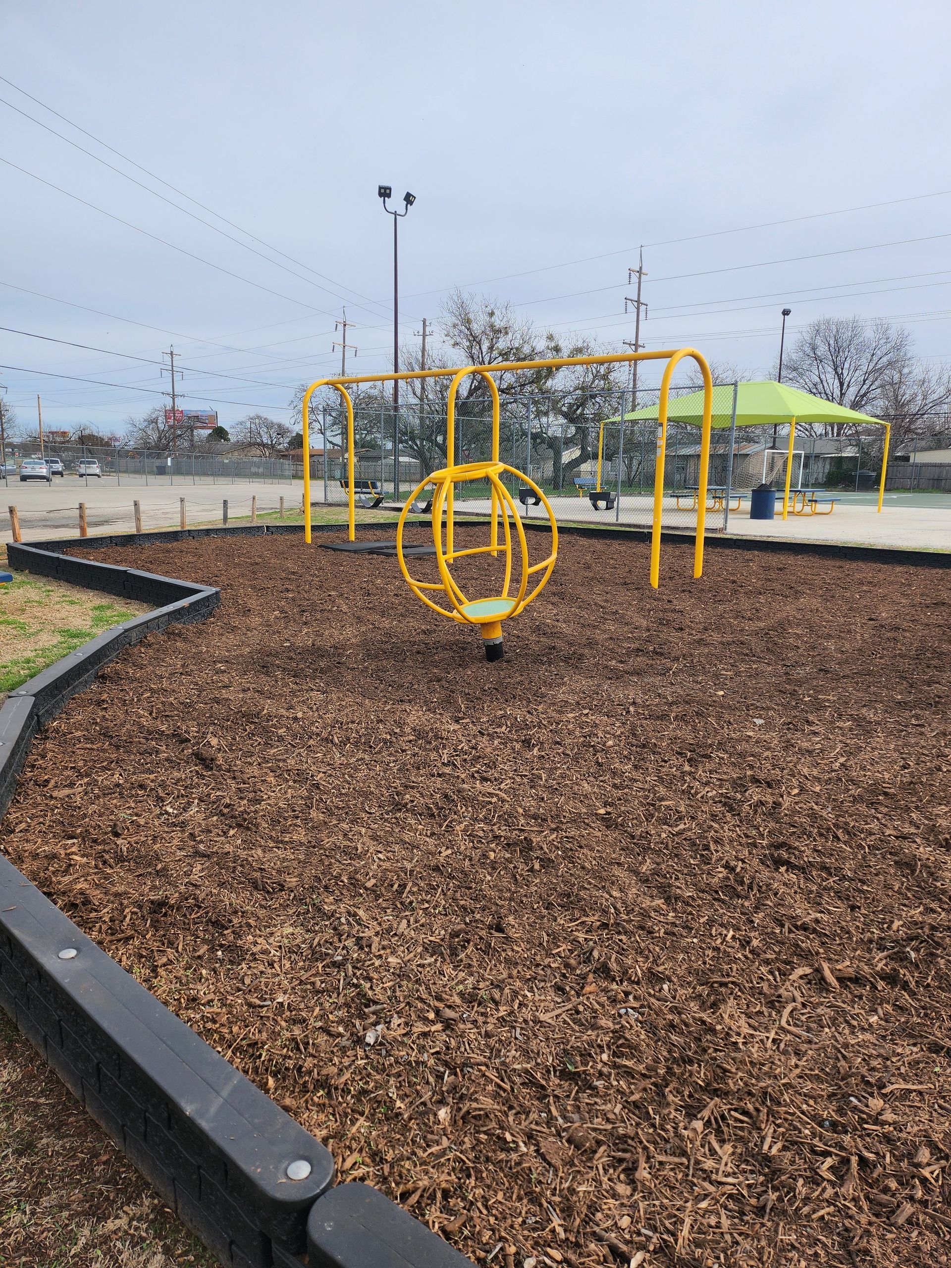 Yellow playground equipment on wood chips at a park on a cloudy day.
