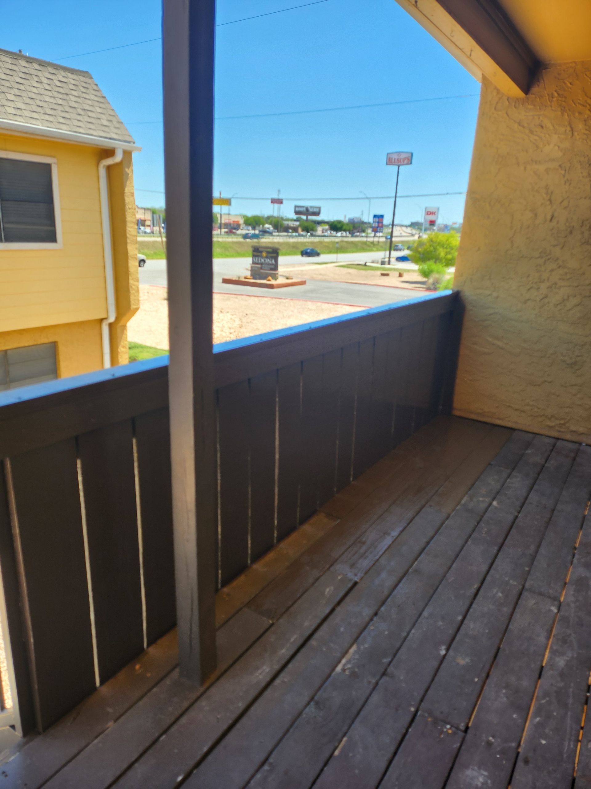 Balcony overlooking a street. Wooden railing, and buildings in the background. Sunny day.