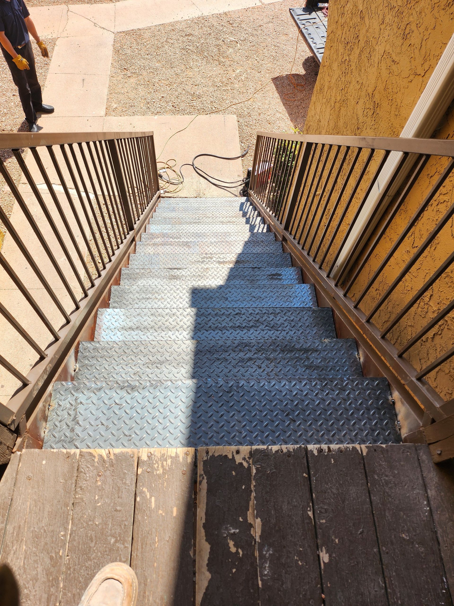 Staircase with metal treads and railings. Person at the top. Yellow building exterior in background.
