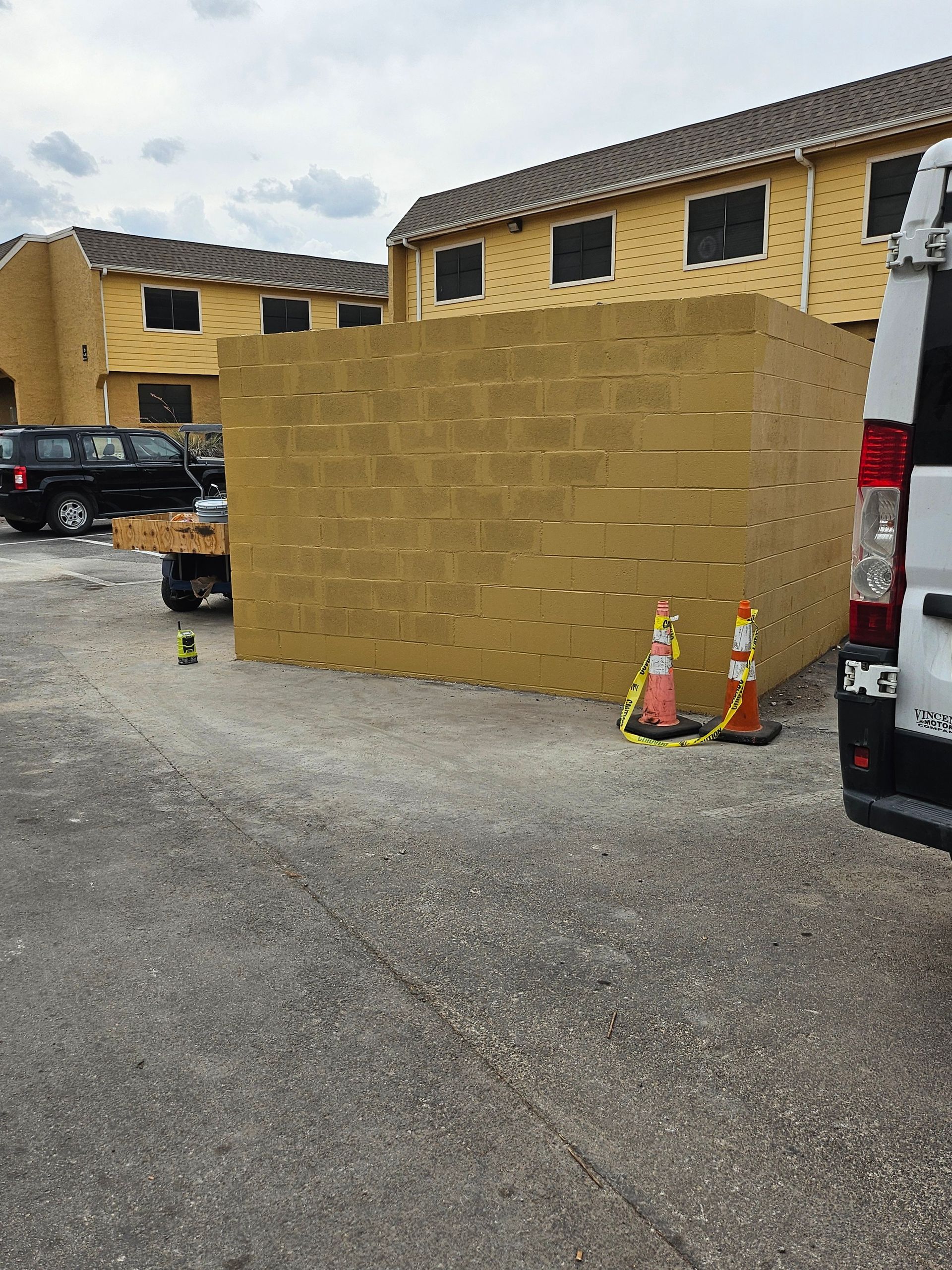 Large rectangular stack of yellow blocks in front of apartment buildings, with traffic cones and vehicles.
