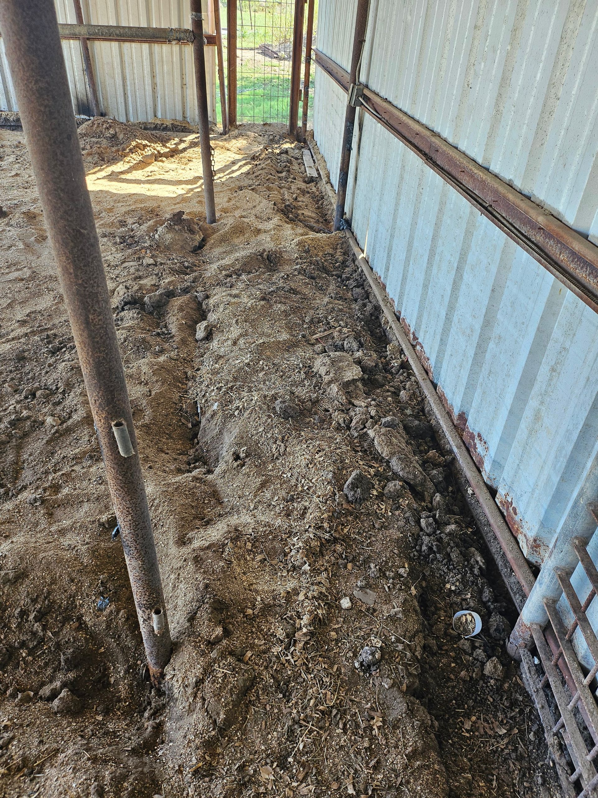 Barn interior with wood shavings, metal posts, and a corrugated metal wall.