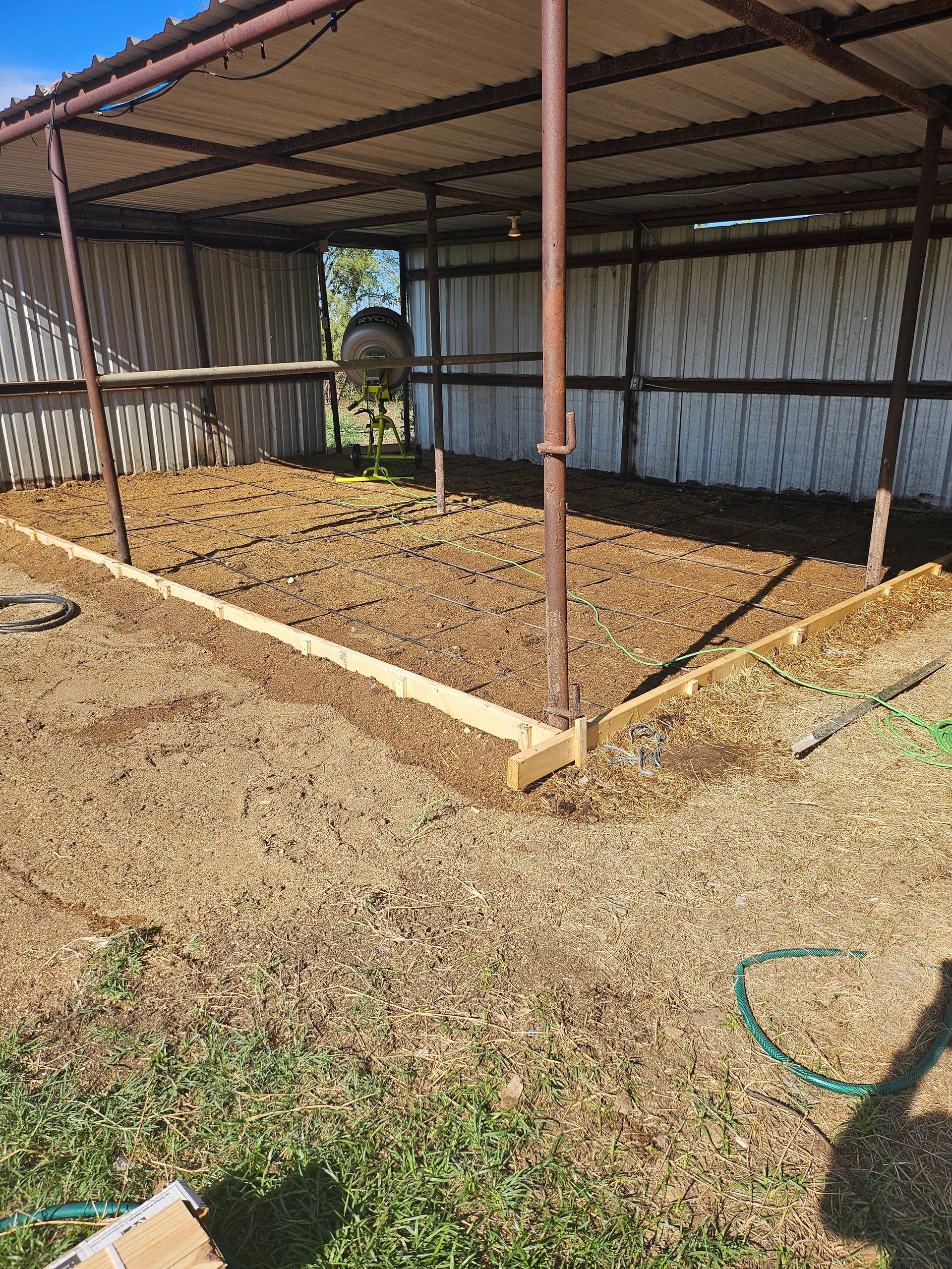 Open-air barn with wood border, metal roof, and dirt floor; brown mulch covers the interior.