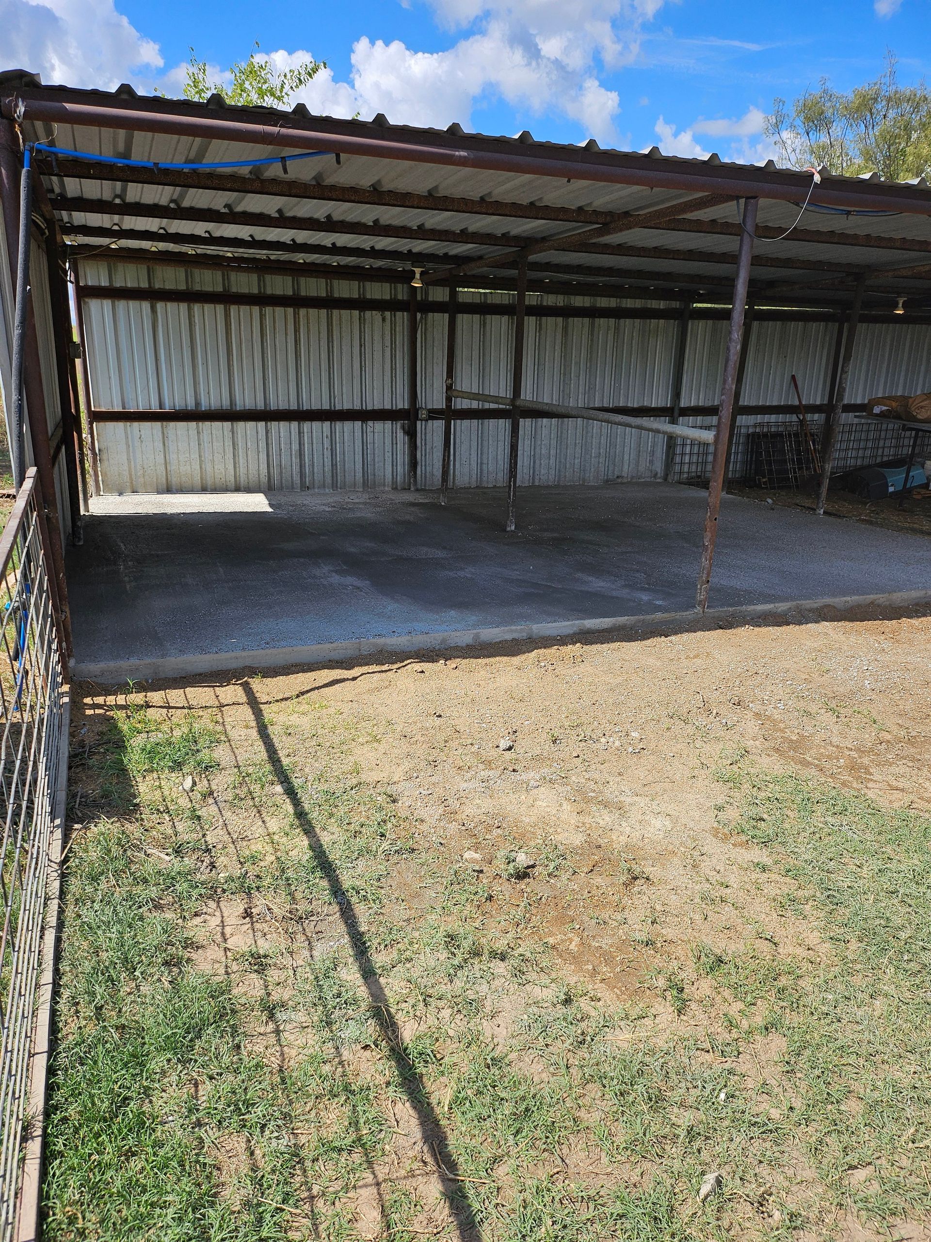 Metal shed with concrete floor and a partially fenced yard.