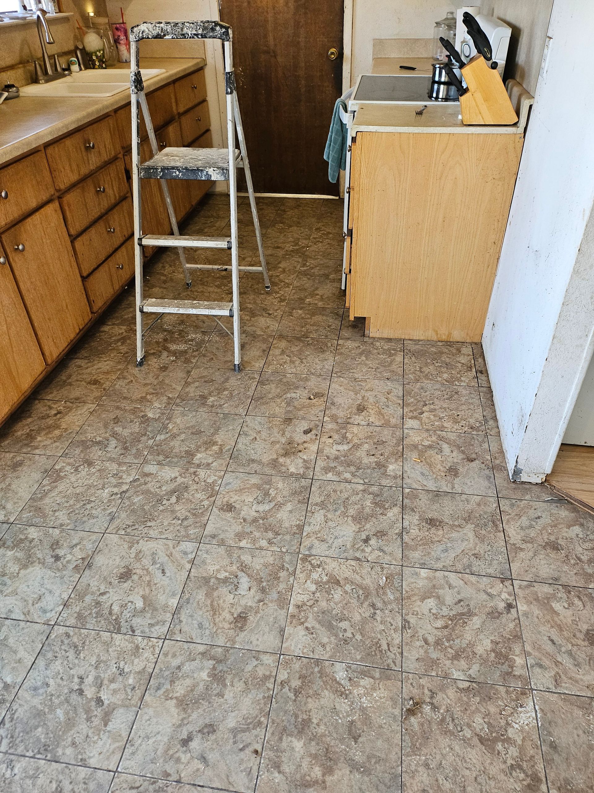 Kitchen with tan speckled flooring, wooden cabinets, ladder, and partially disassembled cabinets.