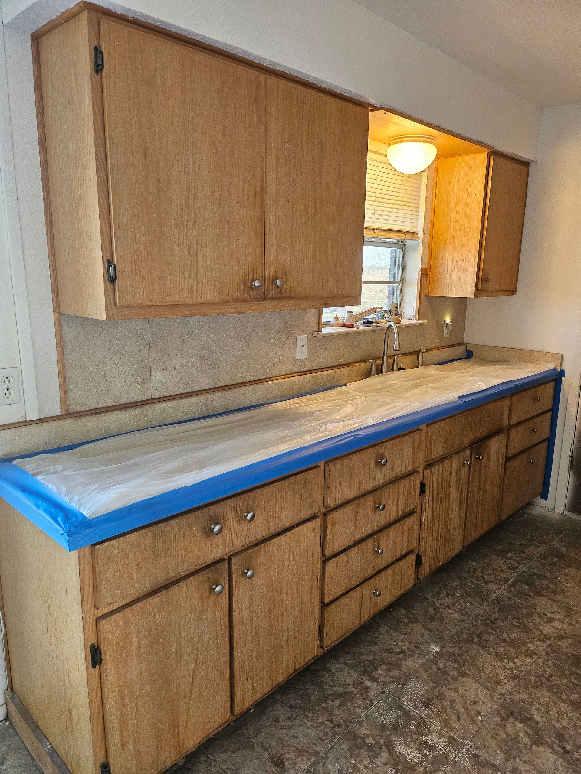 Kitchen cabinets and counter, brown wood, with blue tape along counter edge.