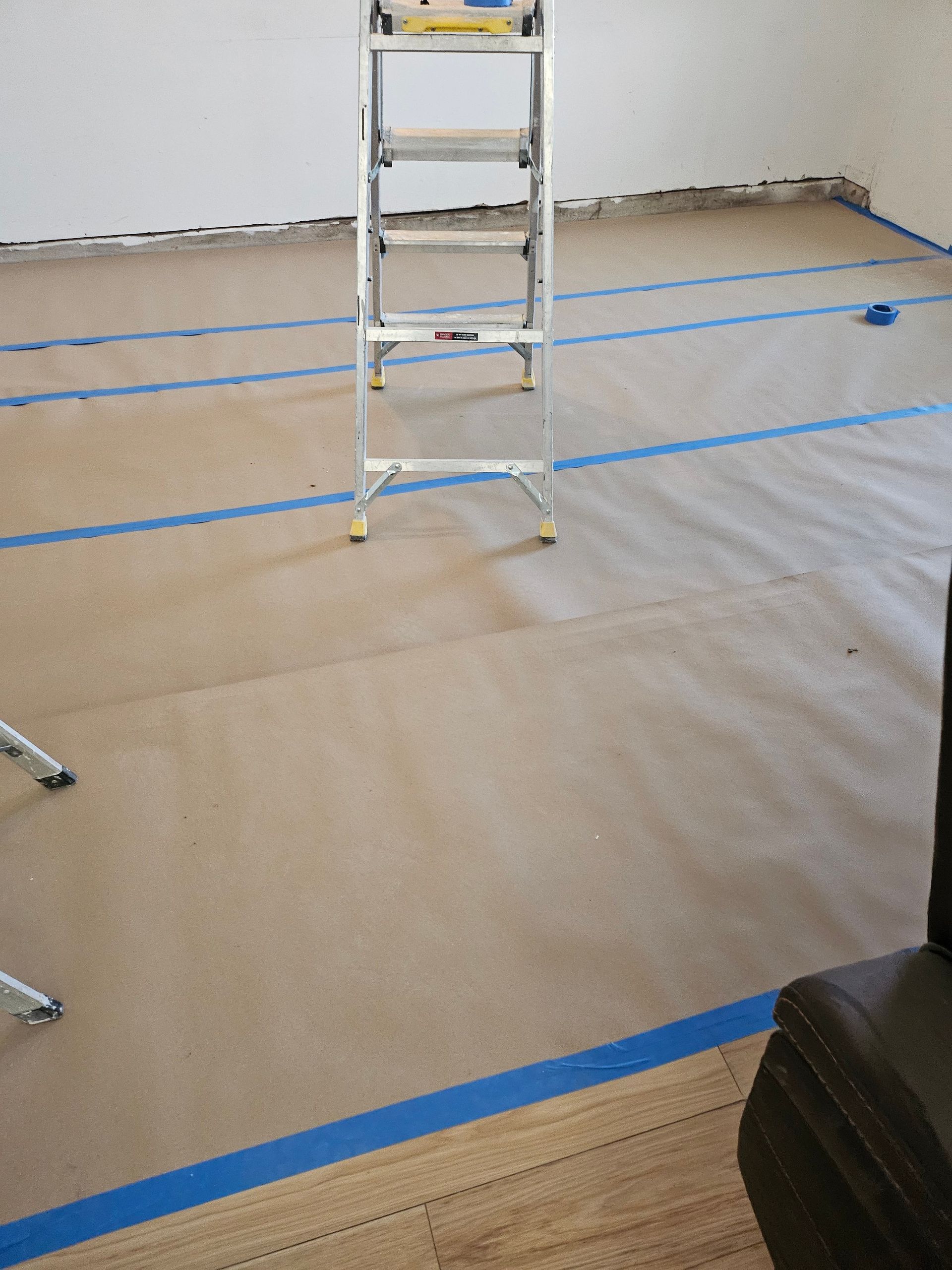 Ladder on paper-covered floor, with blue tape. Room interior, prepping for painting.