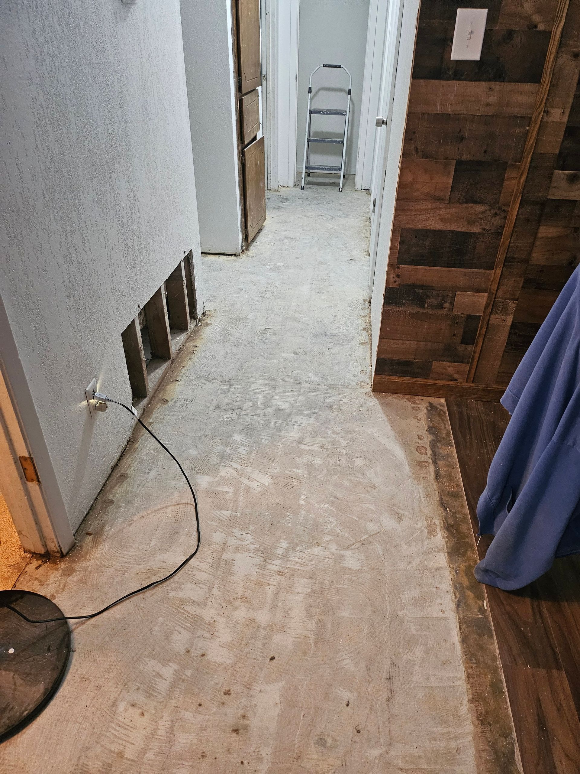 Hallway with bare concrete floor; wall has exposed wood studs. A ladder and refrigerator are visible.