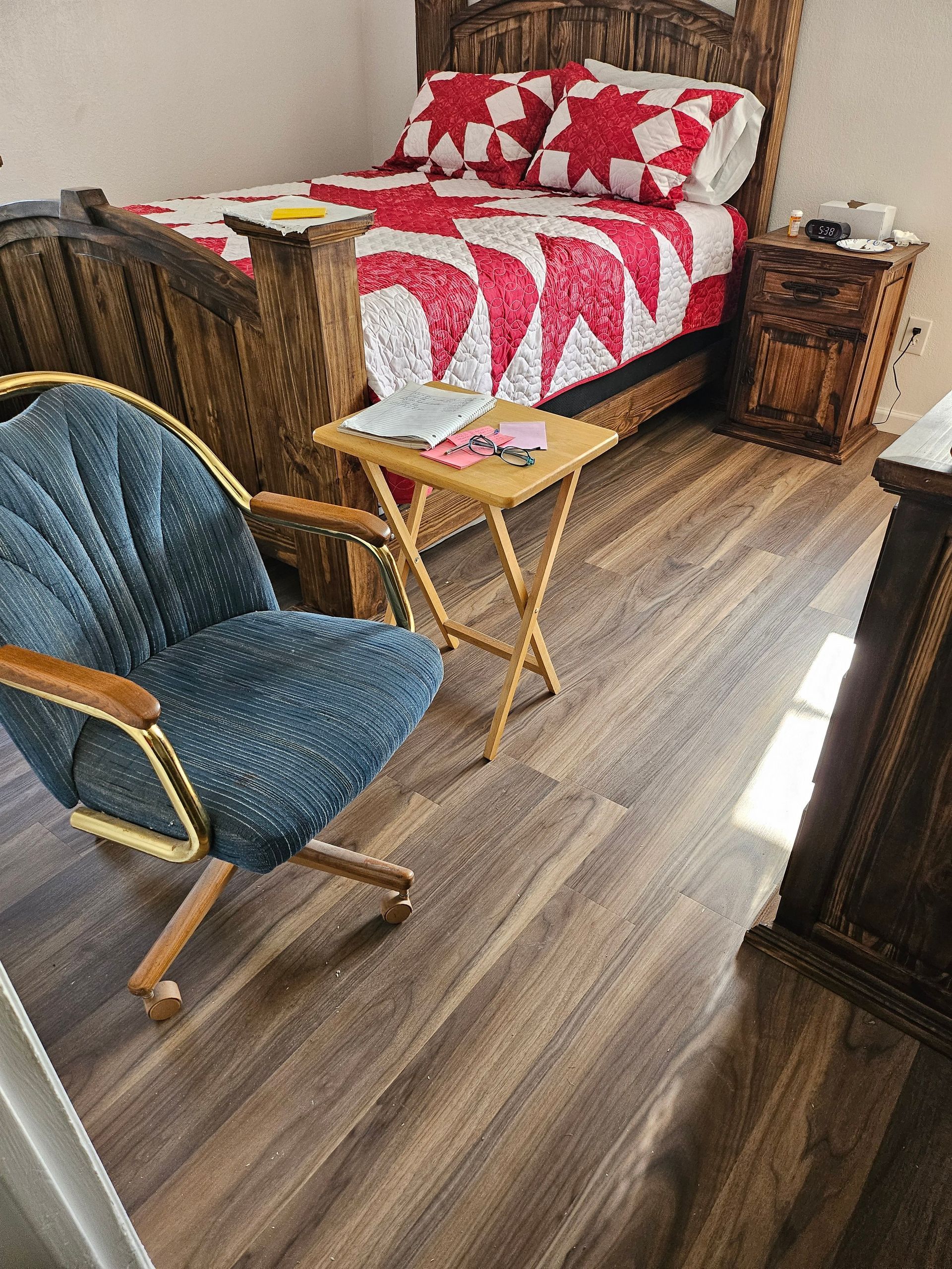Bedroom with wooden furniture and a red and white quilt on the bed. A blue chair sits nearby.